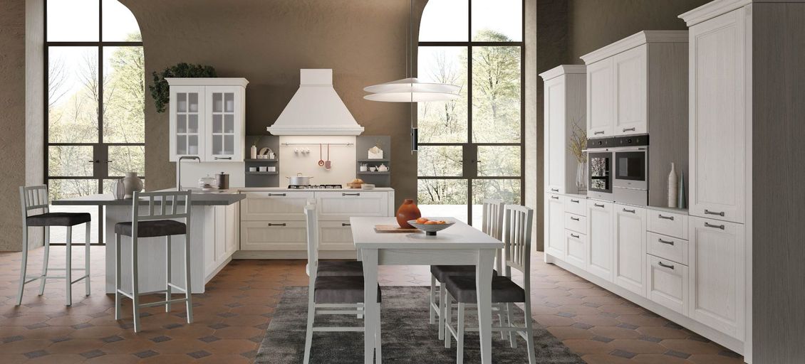 Una cucina con mobili bianchi, tavolo e sedie.