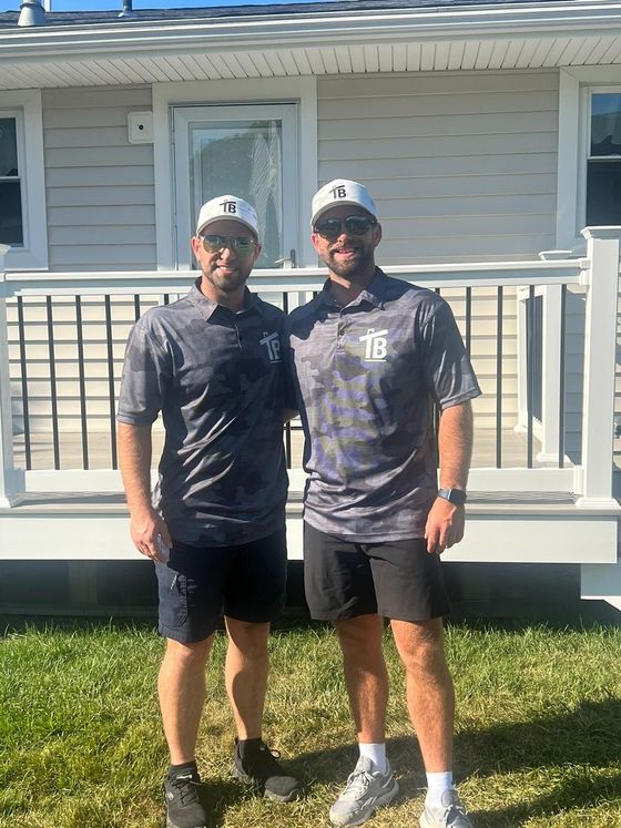 Two men are standing next to each other in front of a house.
