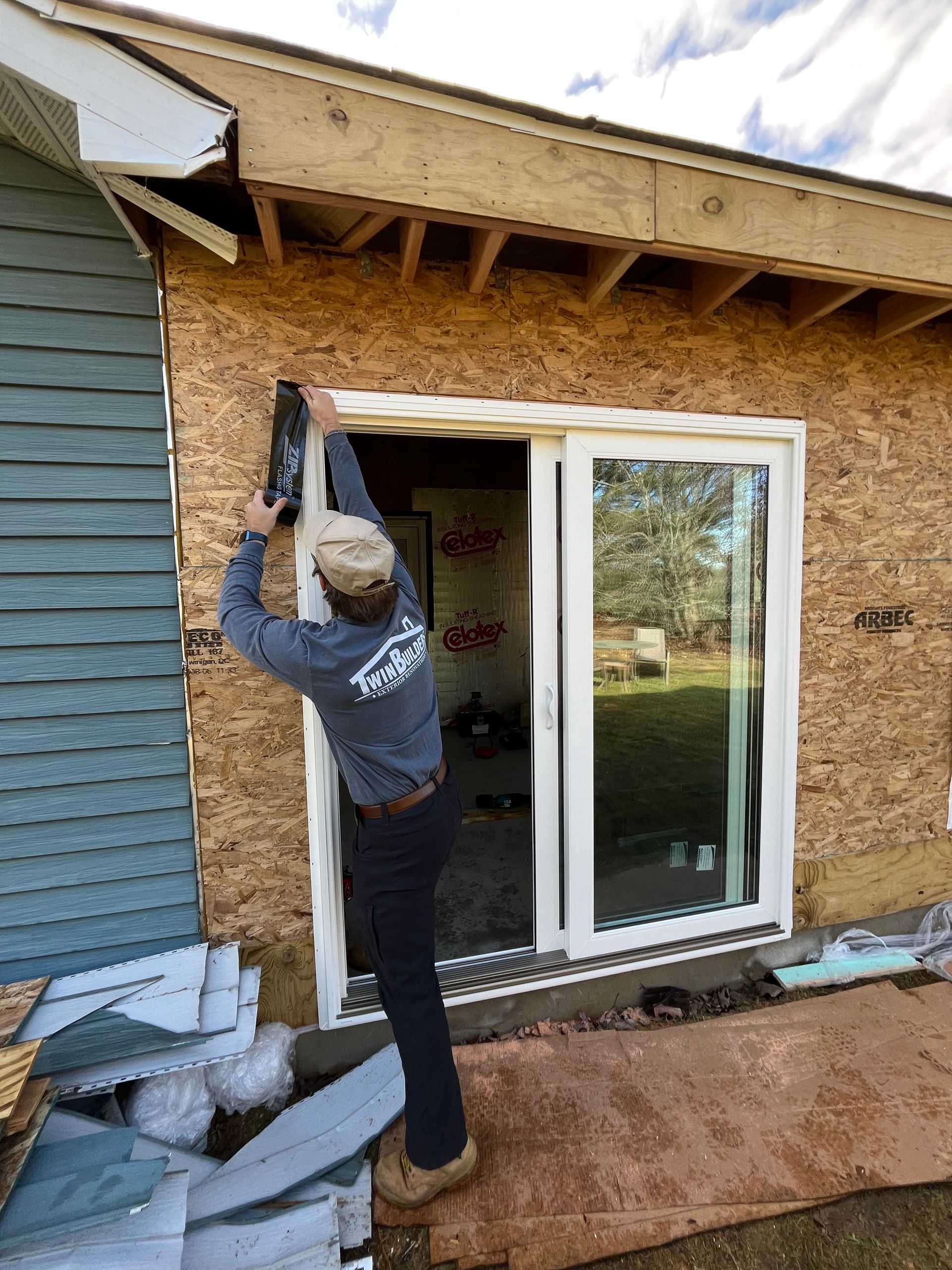 A man is installing a sliding glass door on the side of a house.