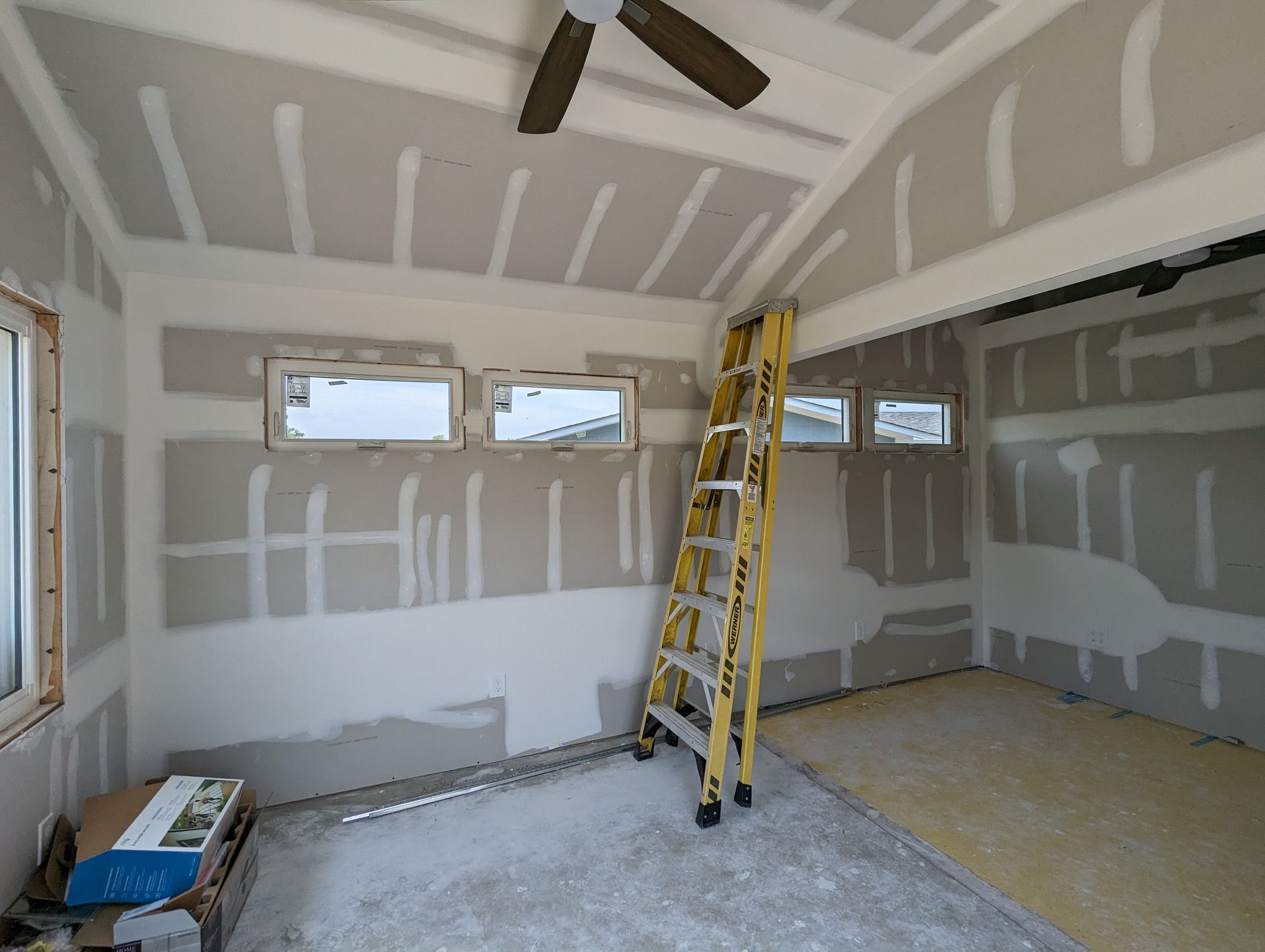 An empty room with a ladder and a ceiling fan