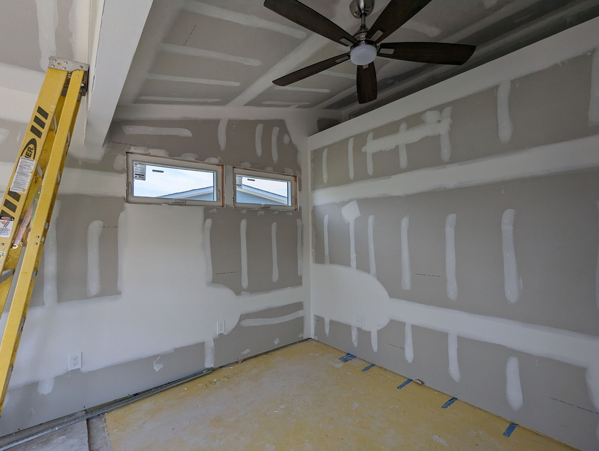 A room with a ceiling fan and a ladder in it