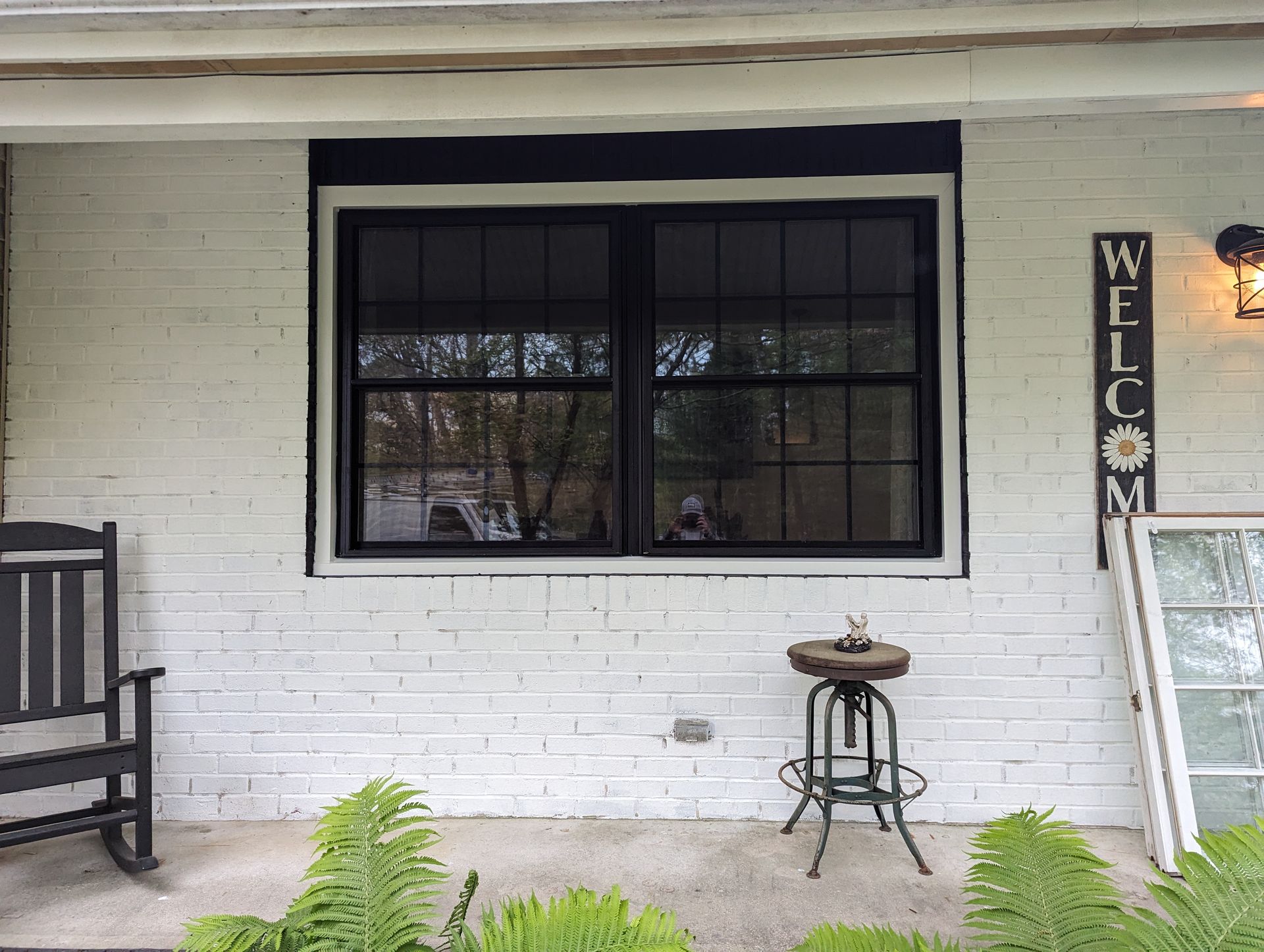 A black rocking chair is on the porch of a white brick house.