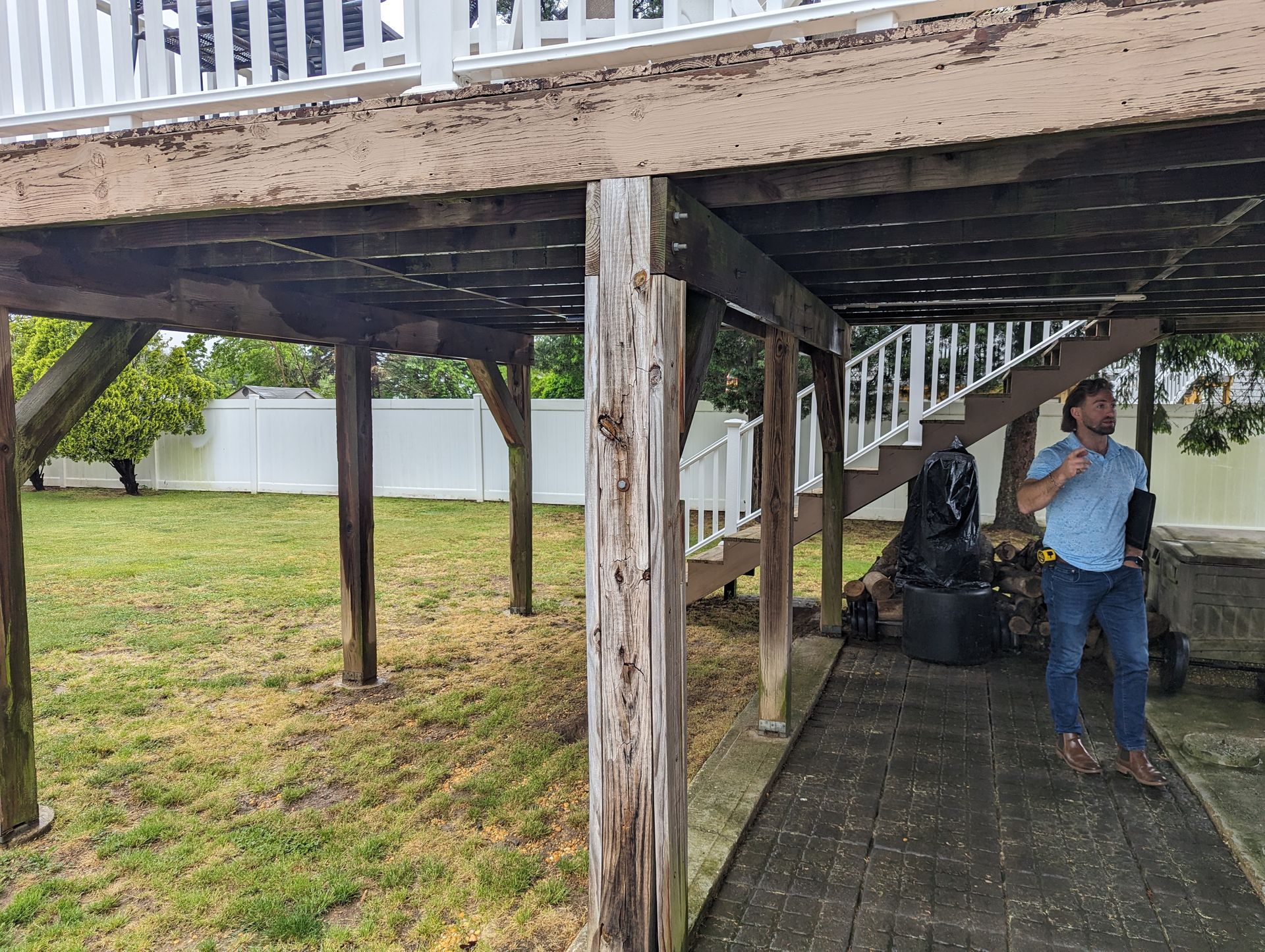 A man is standing under a wooden deck with stairs.