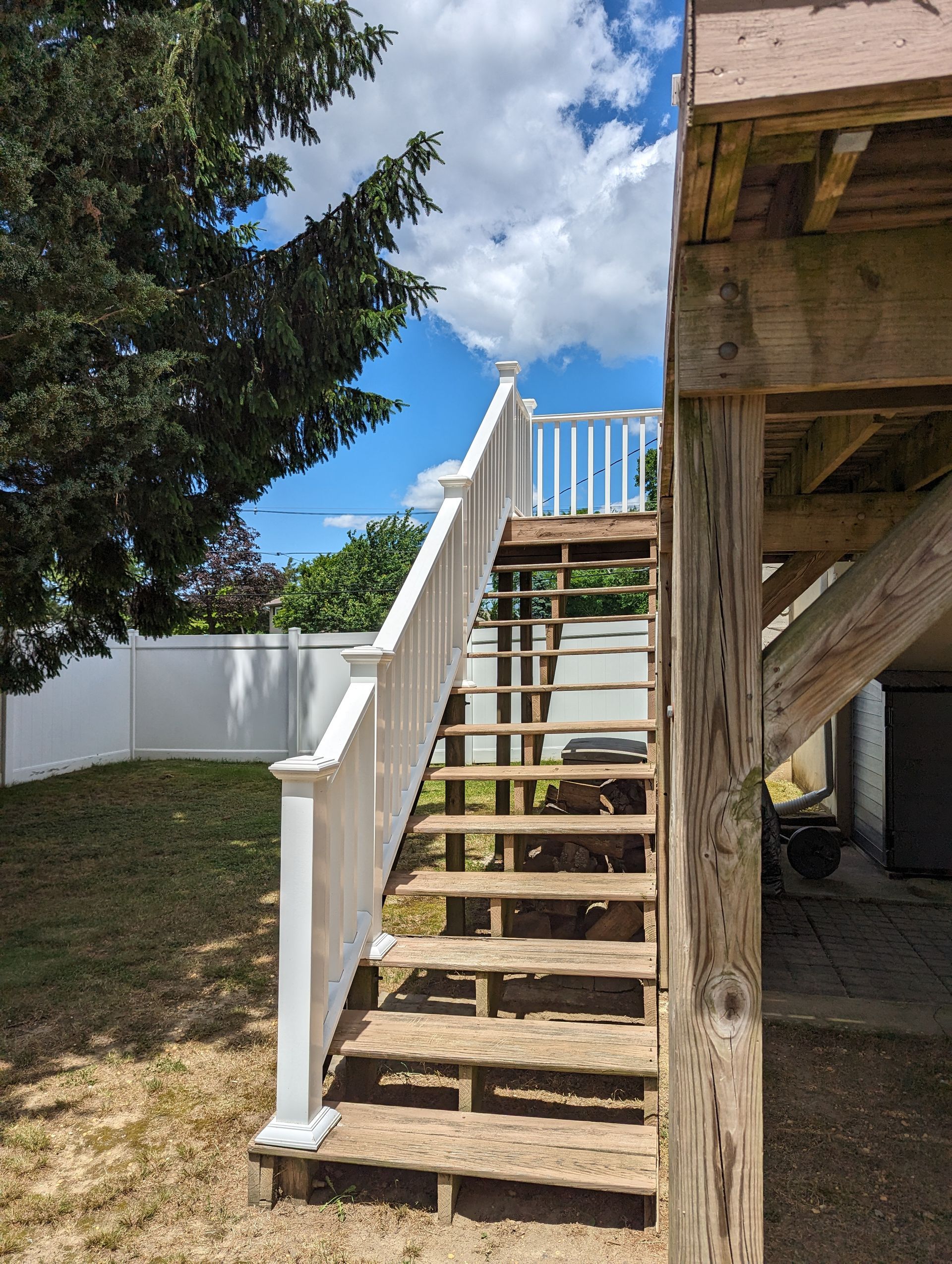 A wooden deck with stairs leading up to it and a white railing.