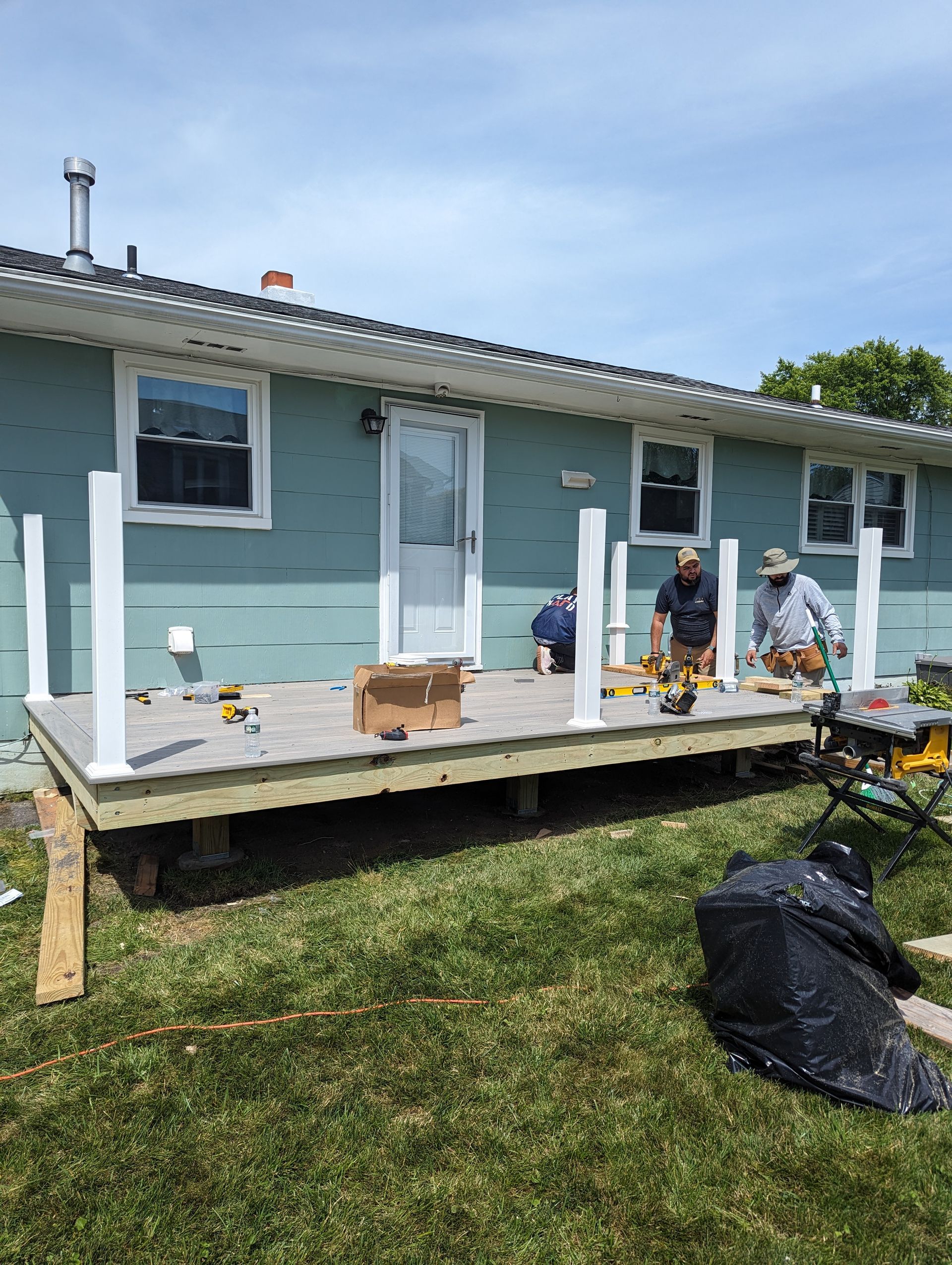Two men are working on a deck in front of a house.