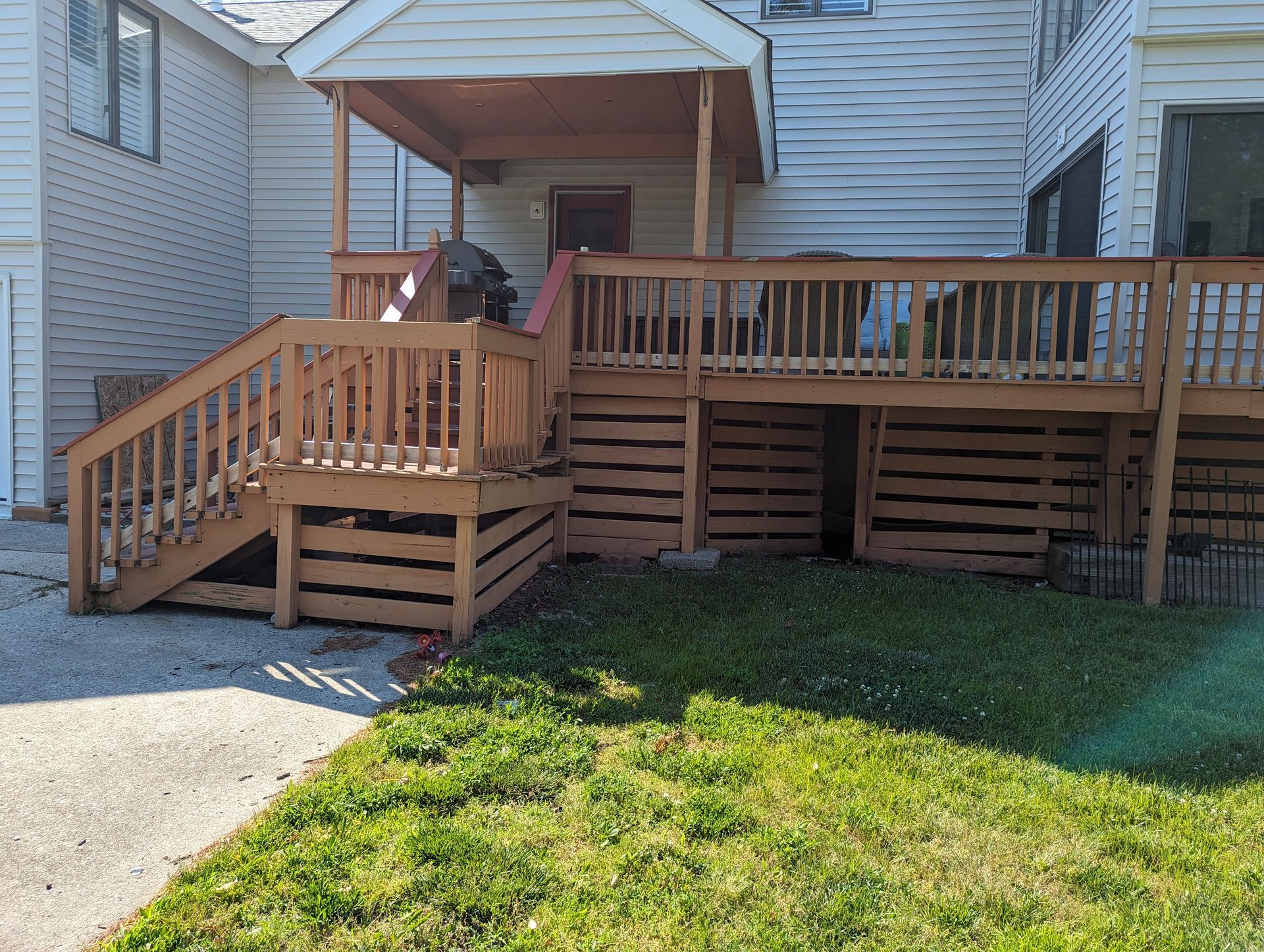 A wooden deck with stairs leading up to it is in front of a white house.