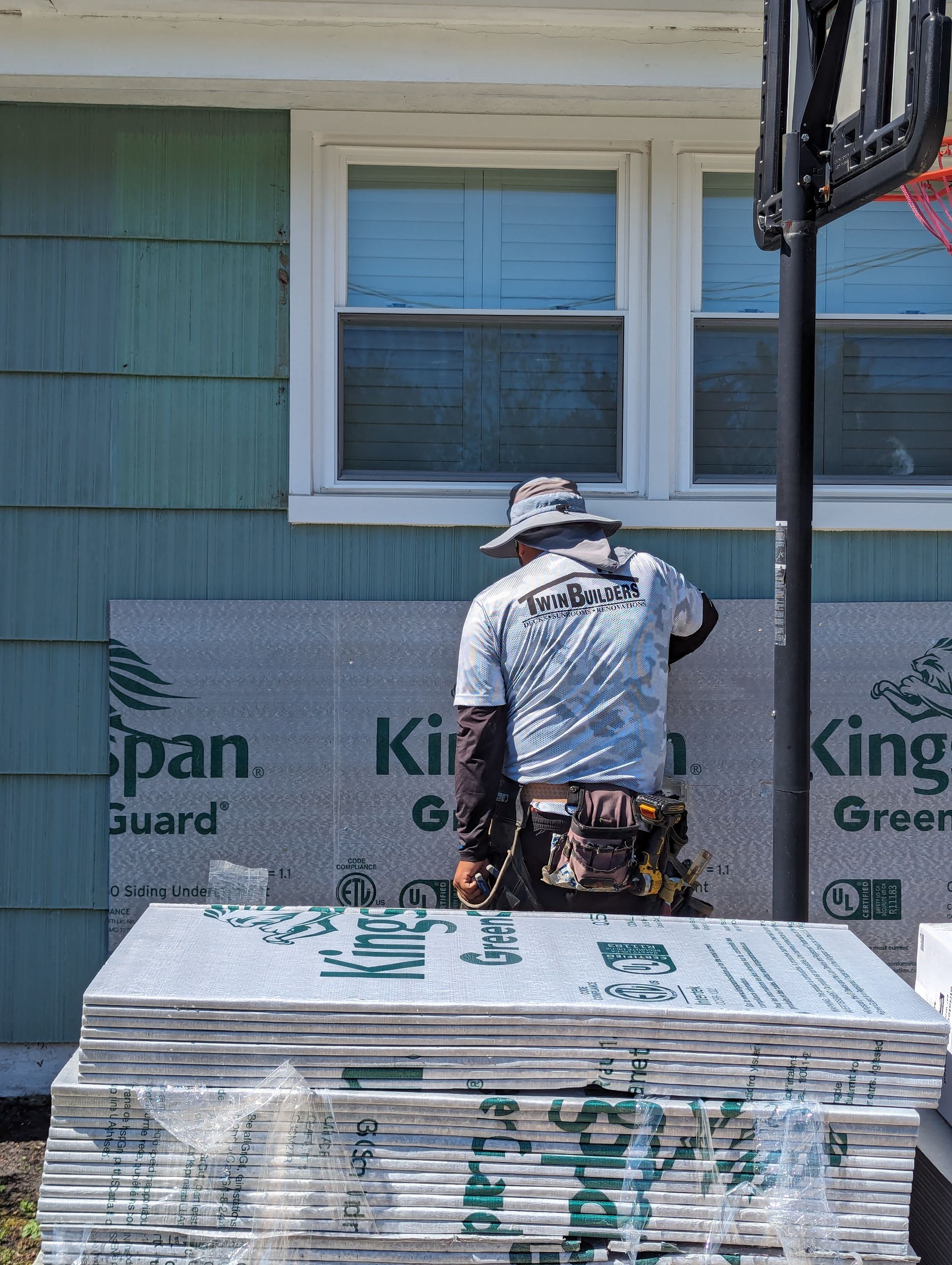 A man is standing in front of a house next to a stack of insulation.