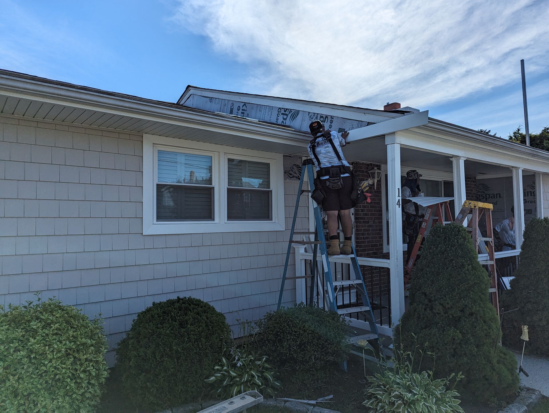 A man is standing on a ladder on the porch of a house.