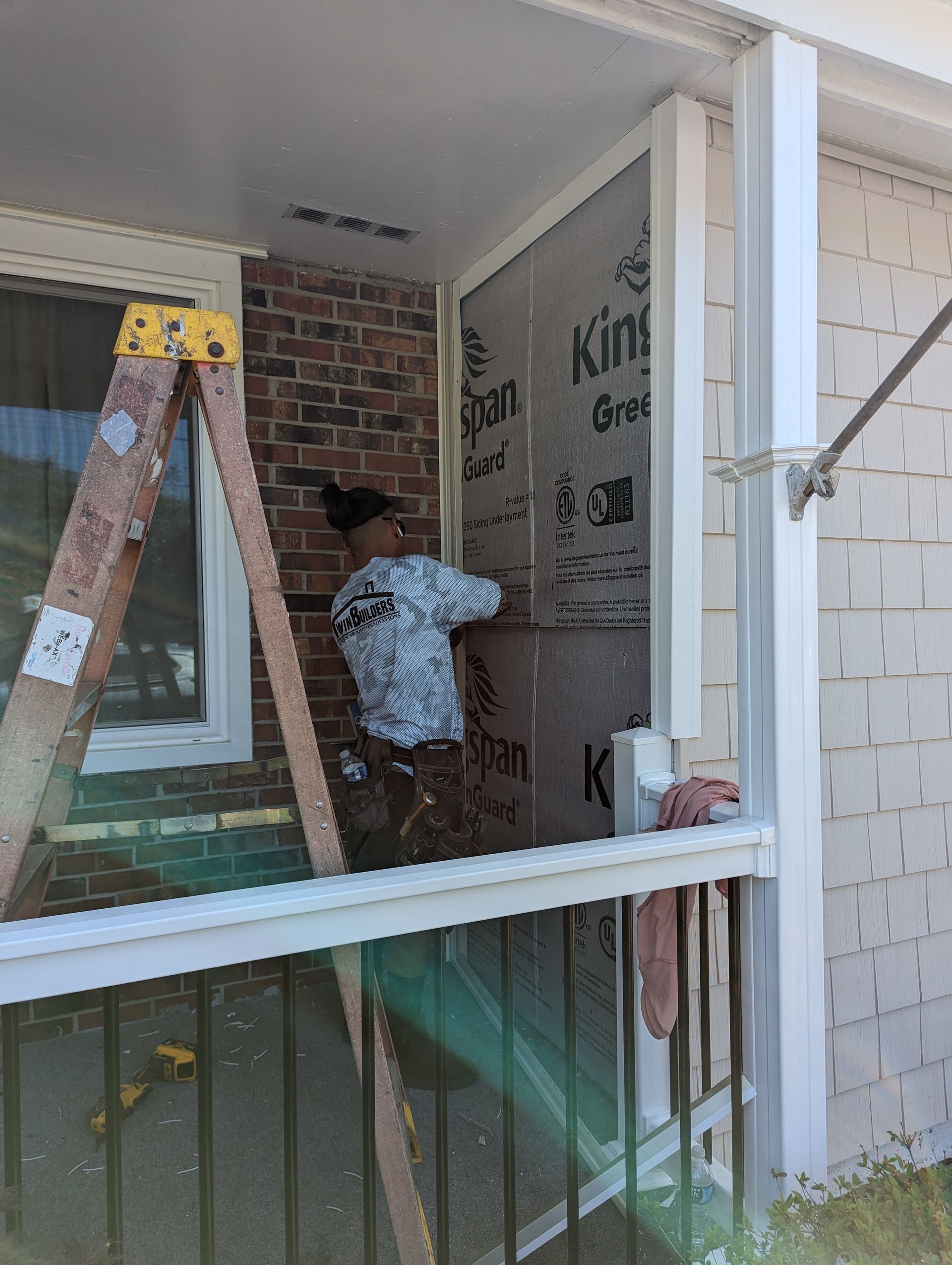 A man is standing on a porch next to a ladder.