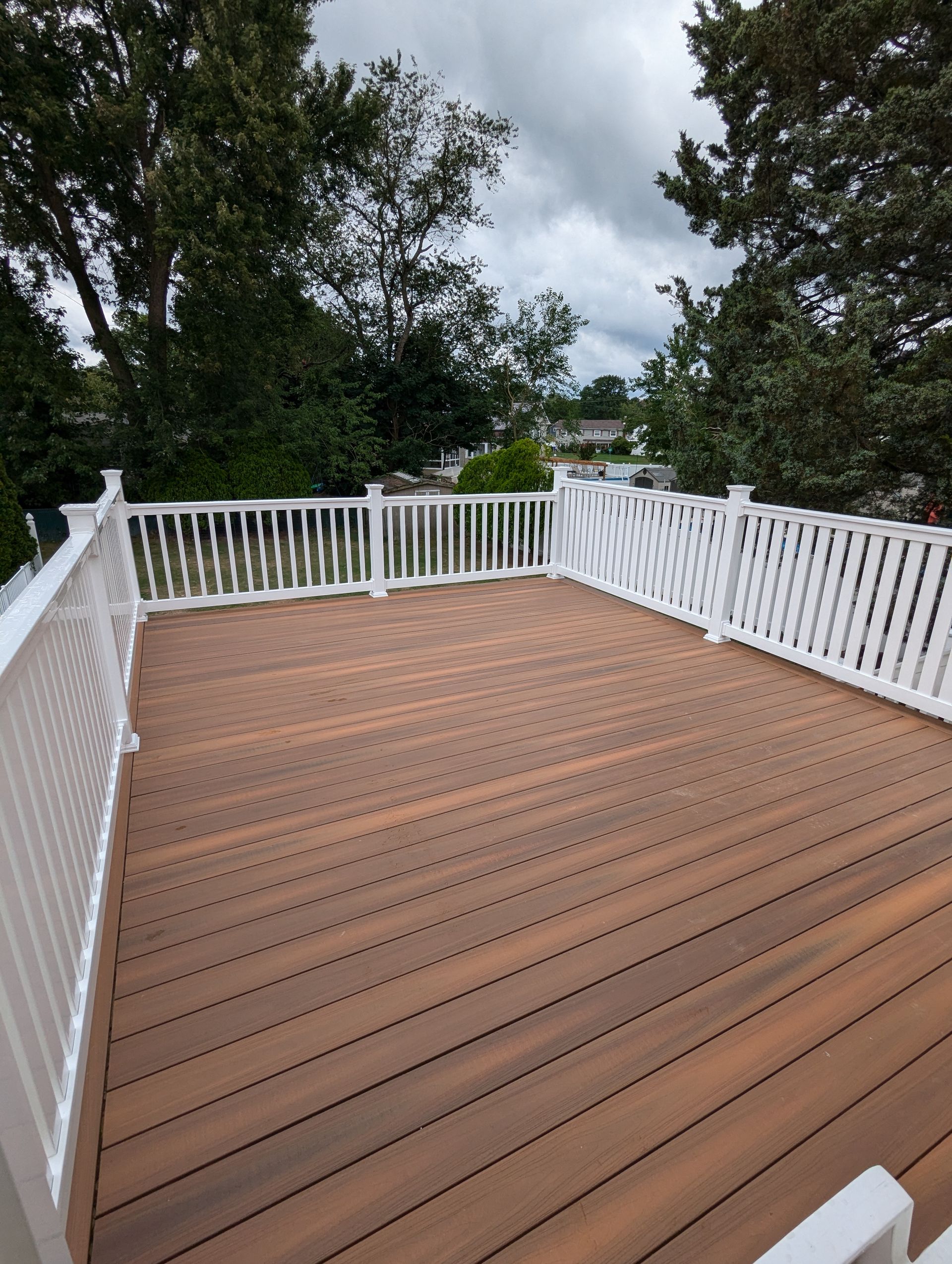 A wooden deck with a white railing and trees in the background.