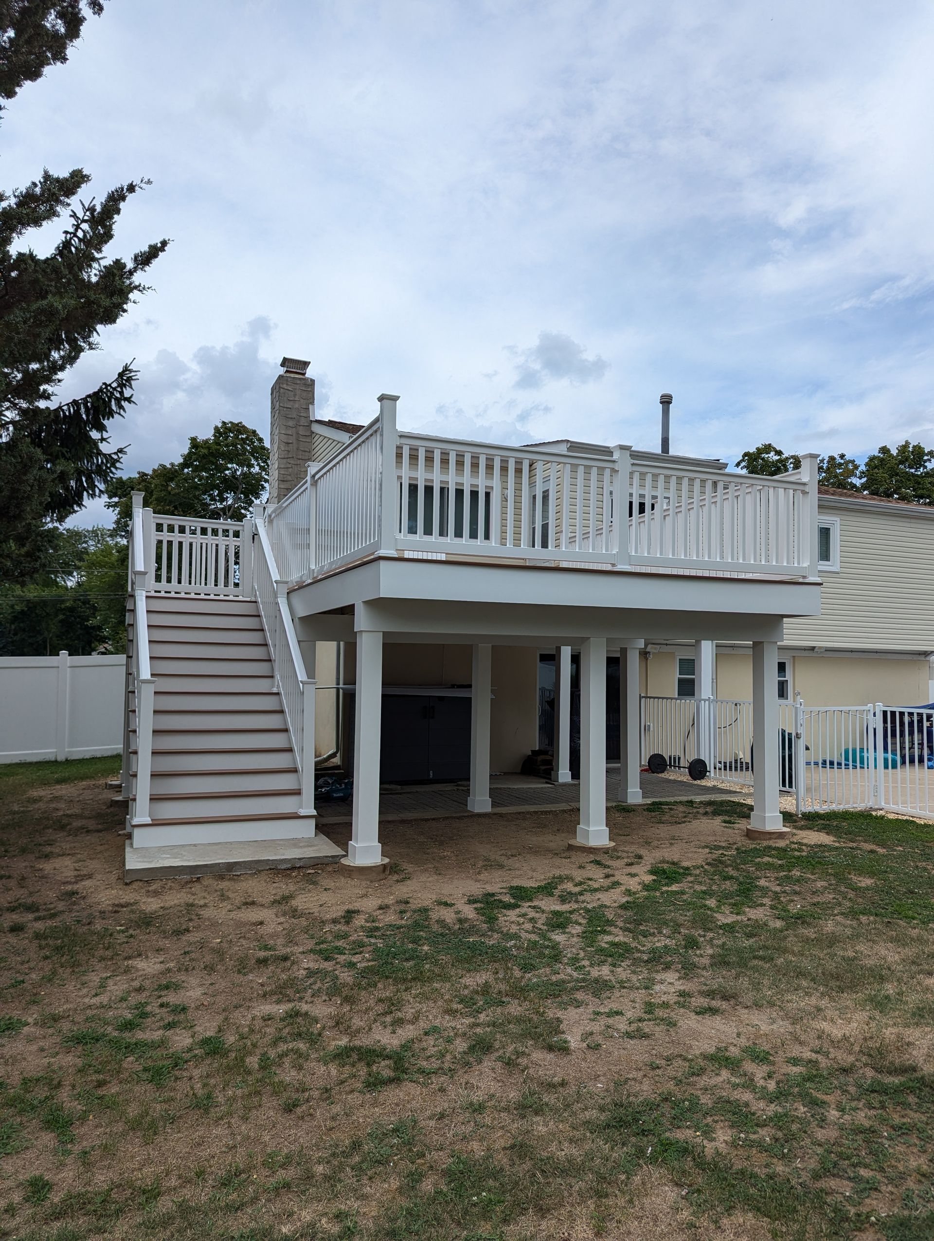 A white deck with stairs leading up to it is in the backyard of a house.