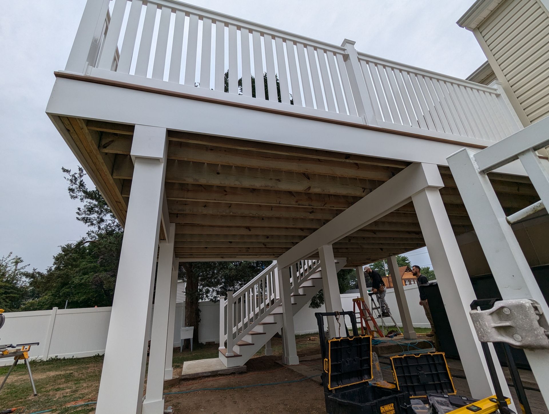 A white deck with stairs leading up to it is under construction.