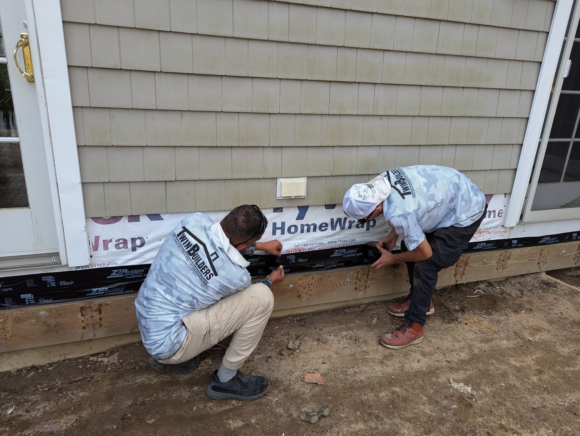 Two men are working on the side of a house.