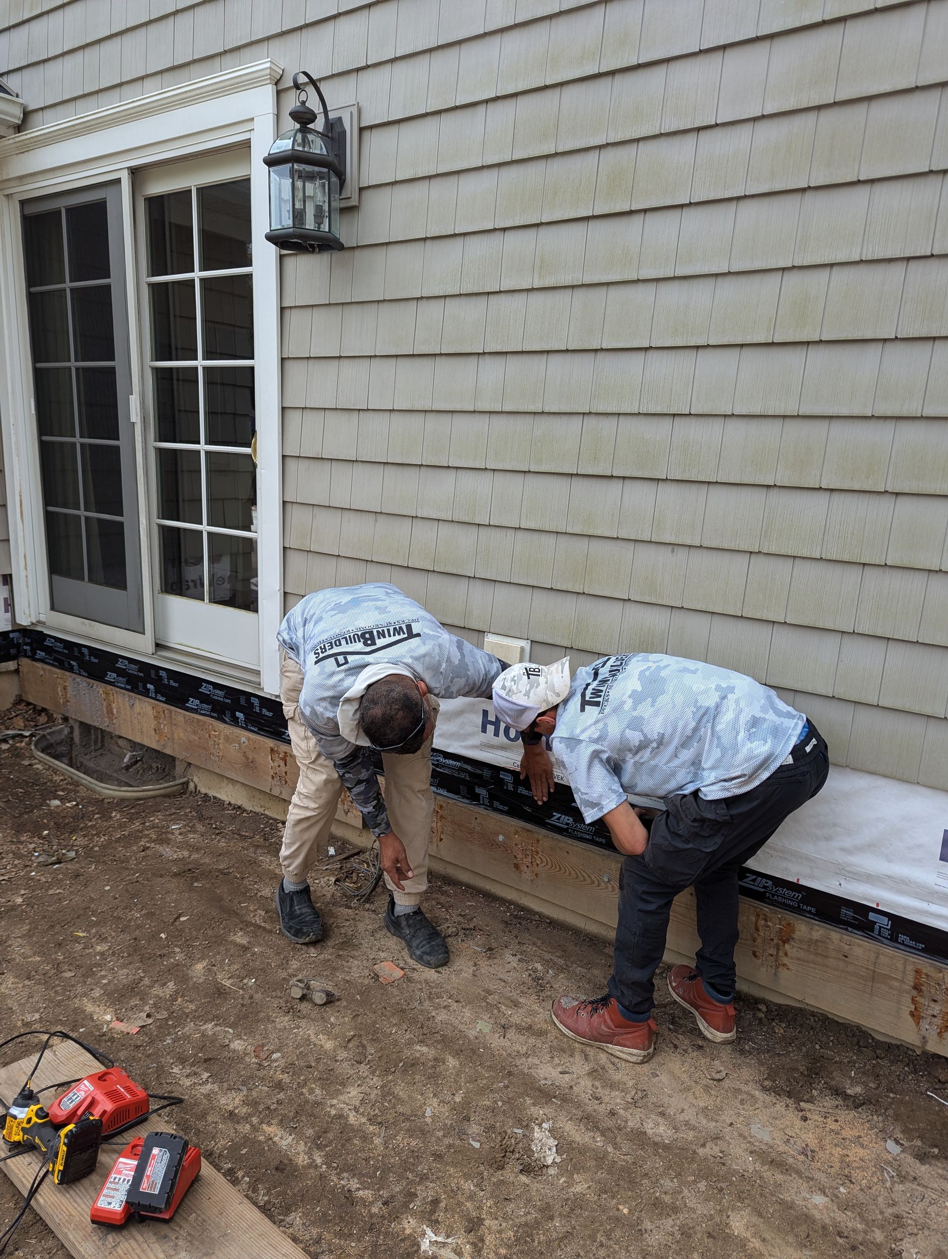 Two men are working on the side of a house.