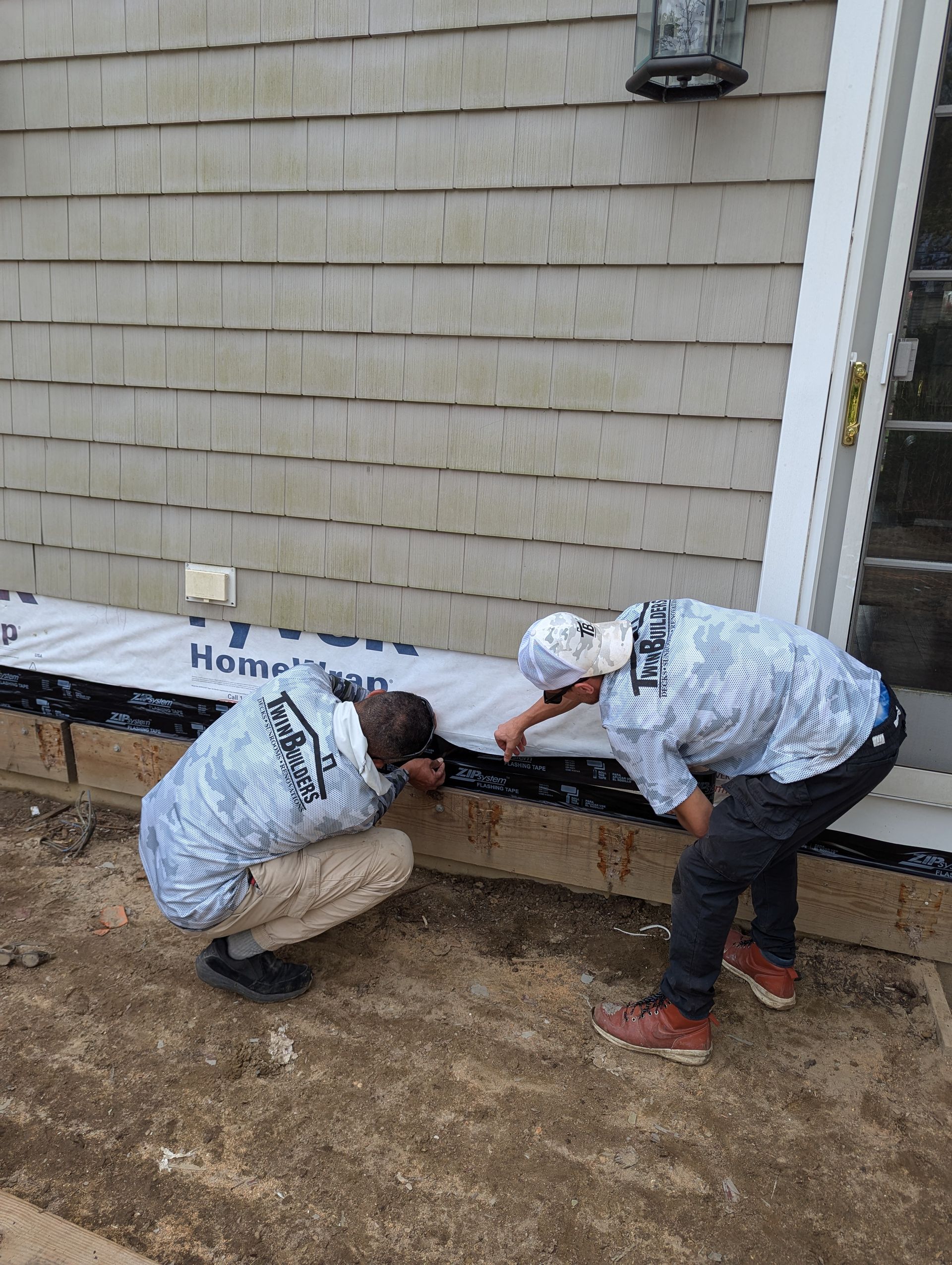 Two men are working on the side of a house.