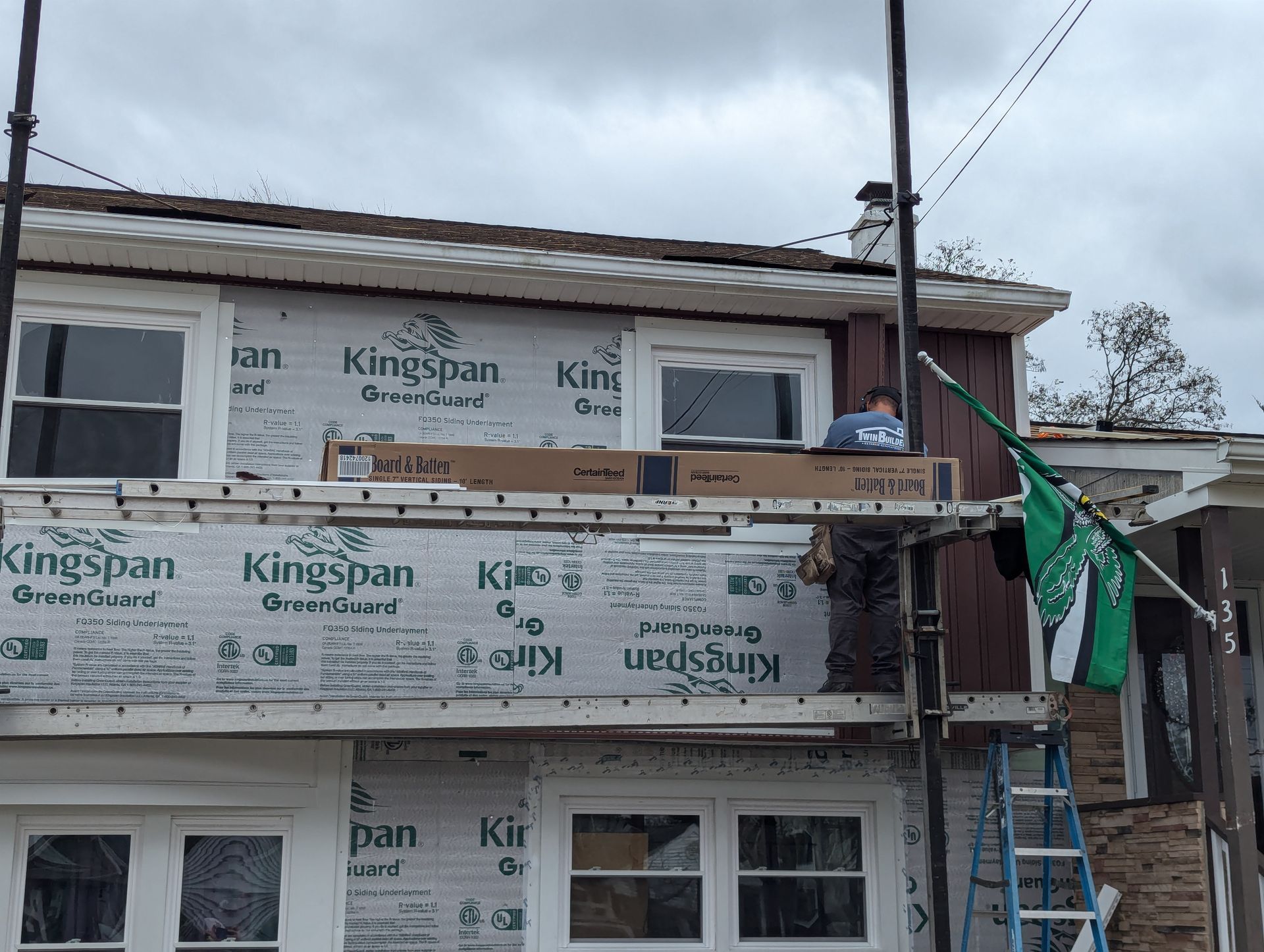 A man is standing on a ladder on the side of a house.