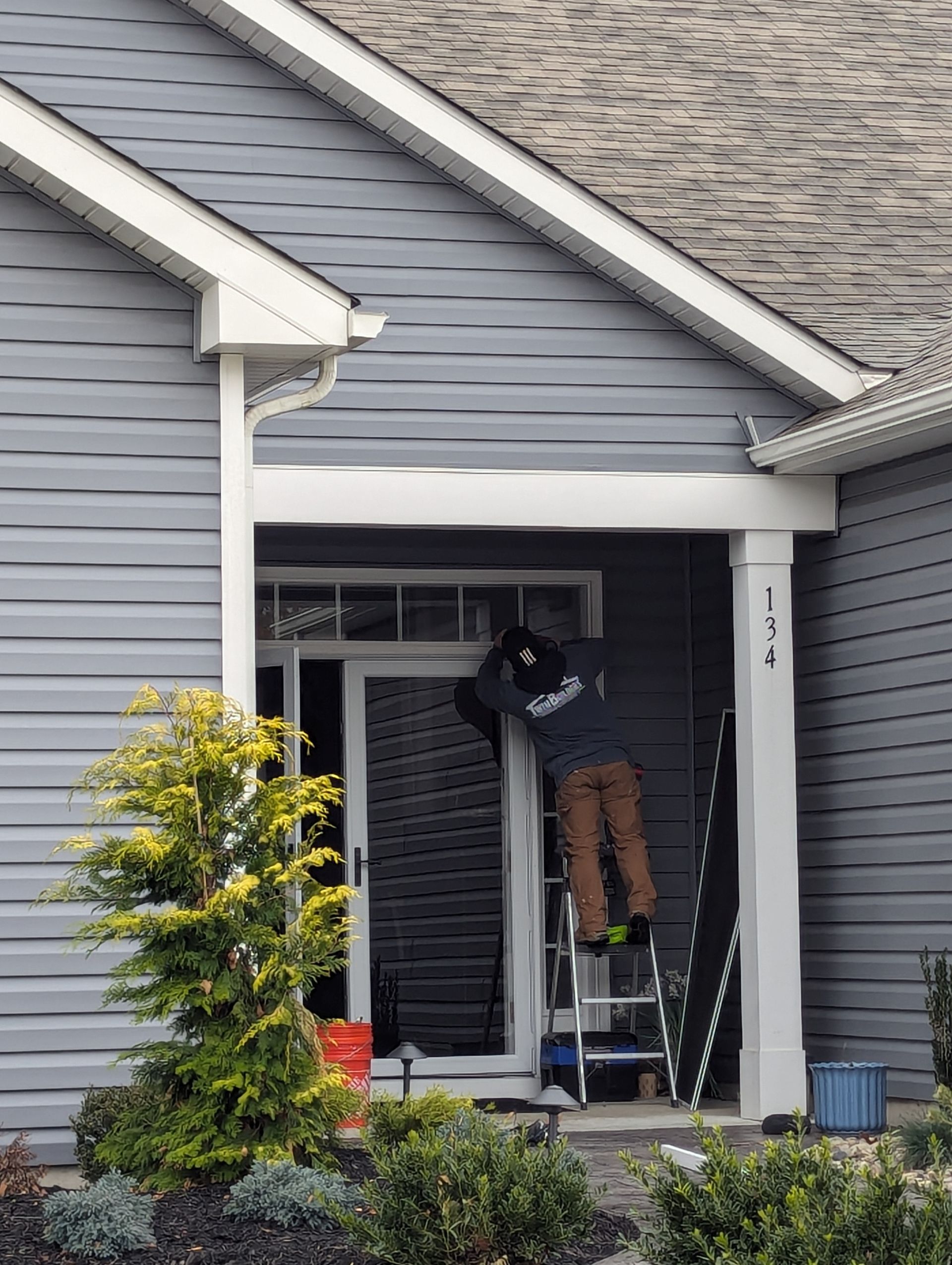 A man is standing on a ladder in front of a house.