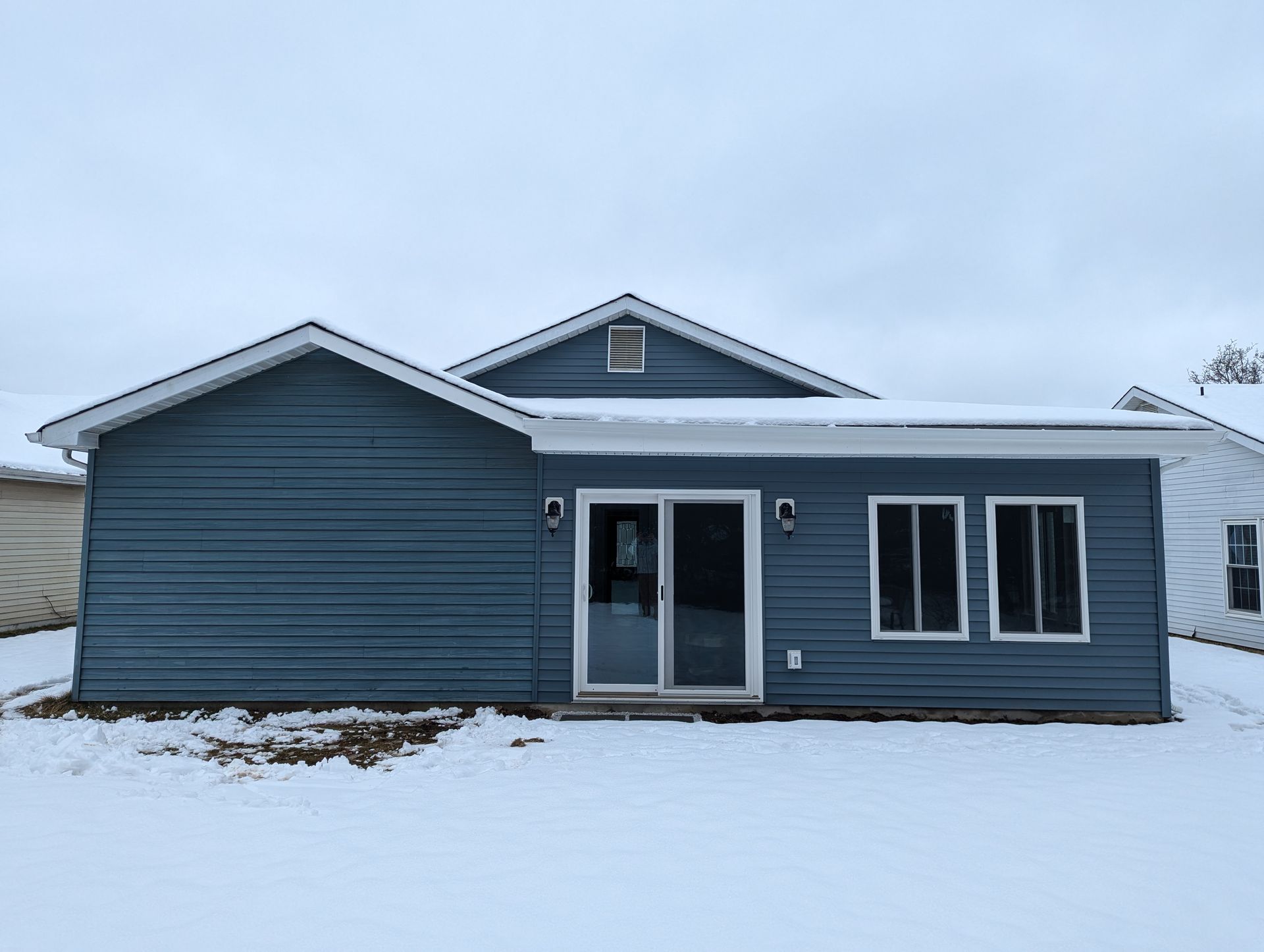 A house with a blue siding and white trim is covered in snow.