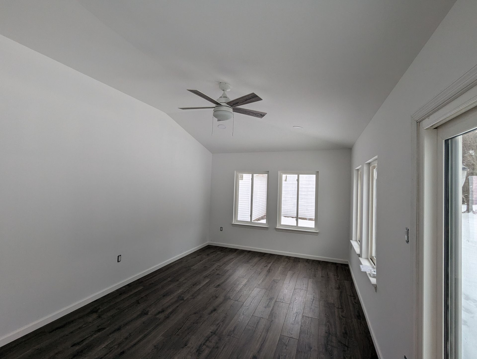 An empty room with hardwood floors and a ceiling fan.