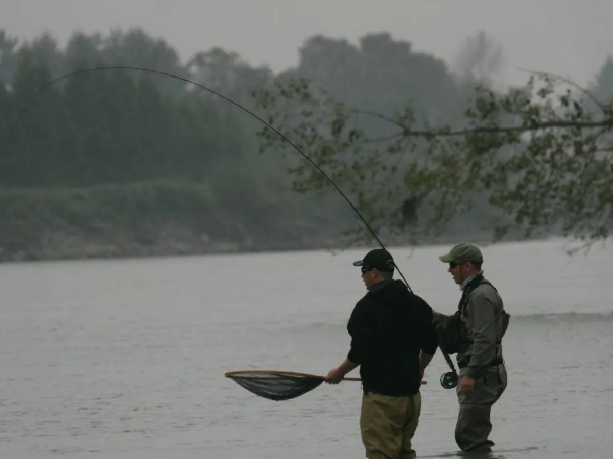 Two men are fishing in the water on a rainy day