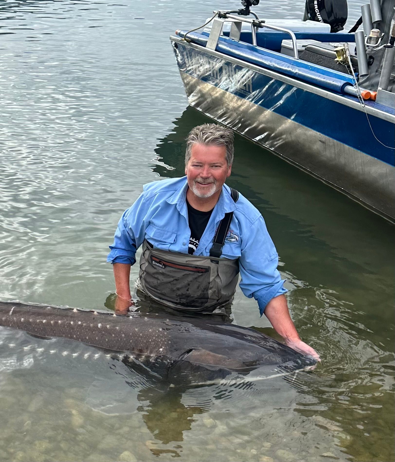 A man is holding a large fish in the water next to a boat.