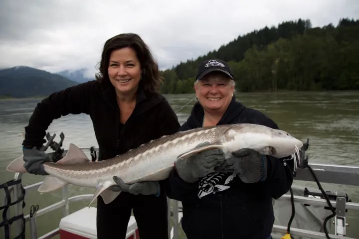 Two women are holding a large fish on a boat.