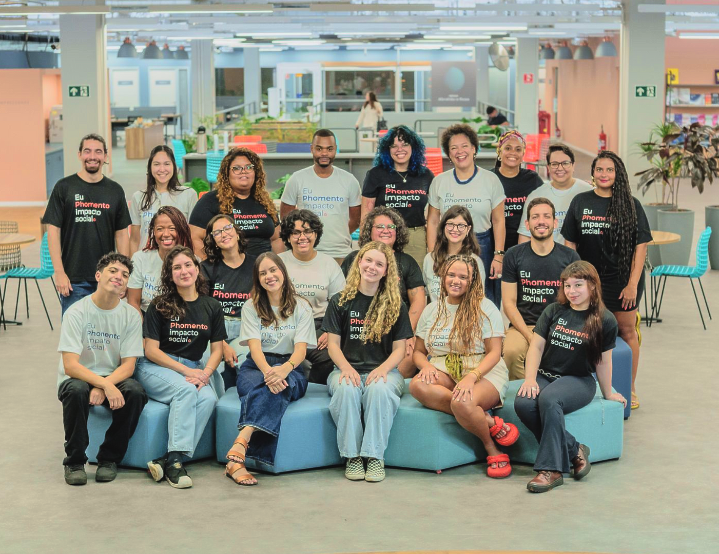 Grupo de pessoas sorridentes posando em sofás azuis em um lounge de escritório iluminado.