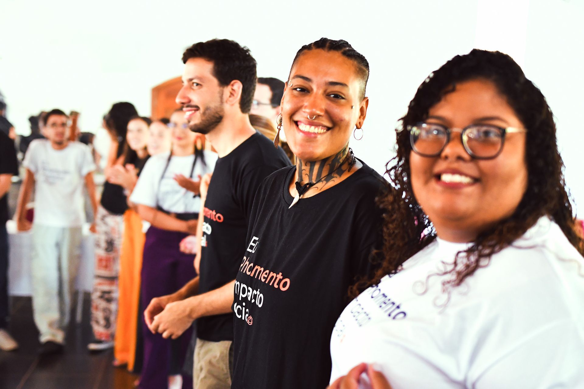 Pessoas sorridentes vestindo camisas pretas e brancas em um espaço interno iluminado para eventos.