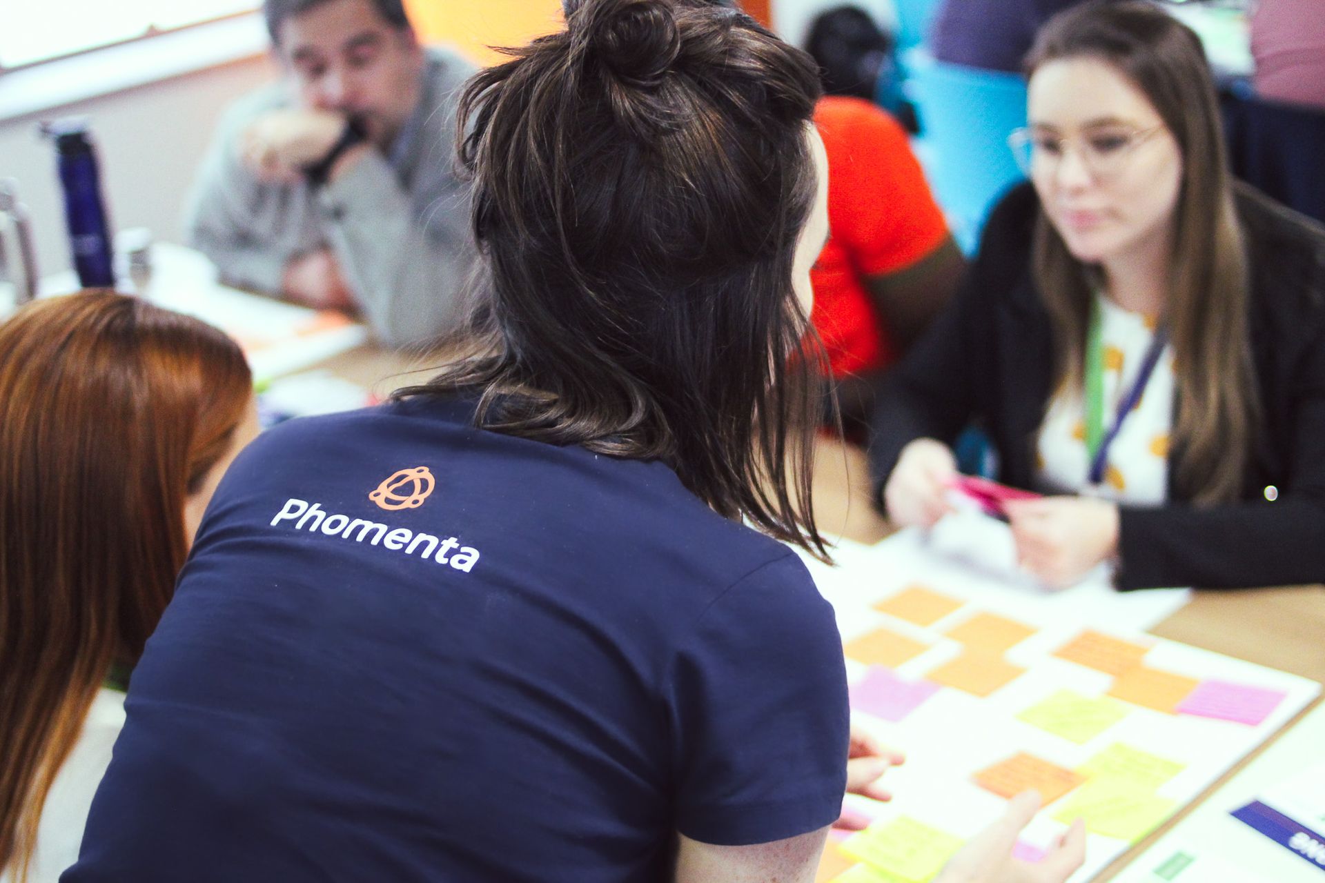 Pessoas colaborando em torno de uma mesa com cartões coloridos, uma delas vestindo uma camisa azul-marinho da Promenta.