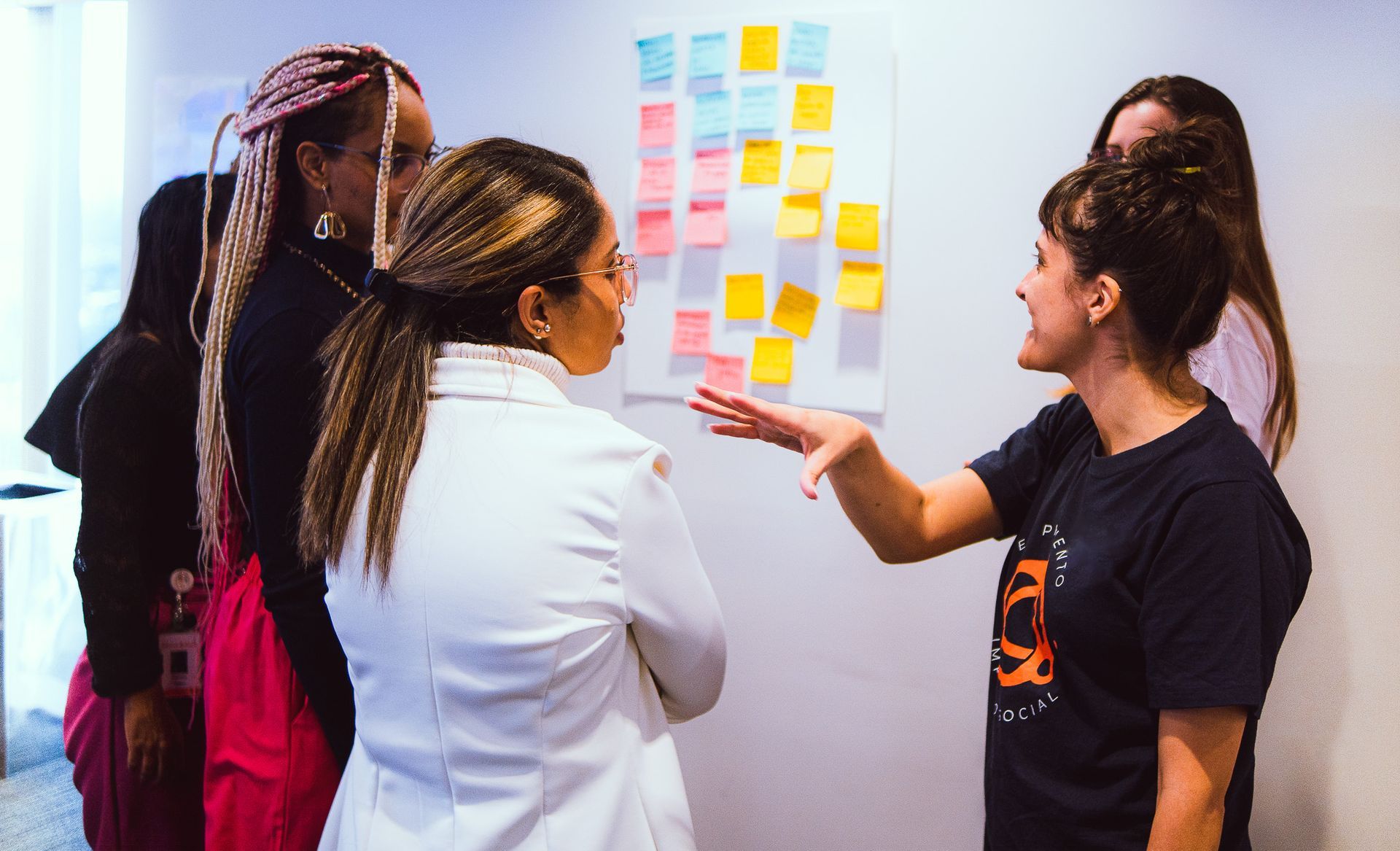 Três pessoas conversando sobre post-its coloridos em uma parede durante uma oficina.