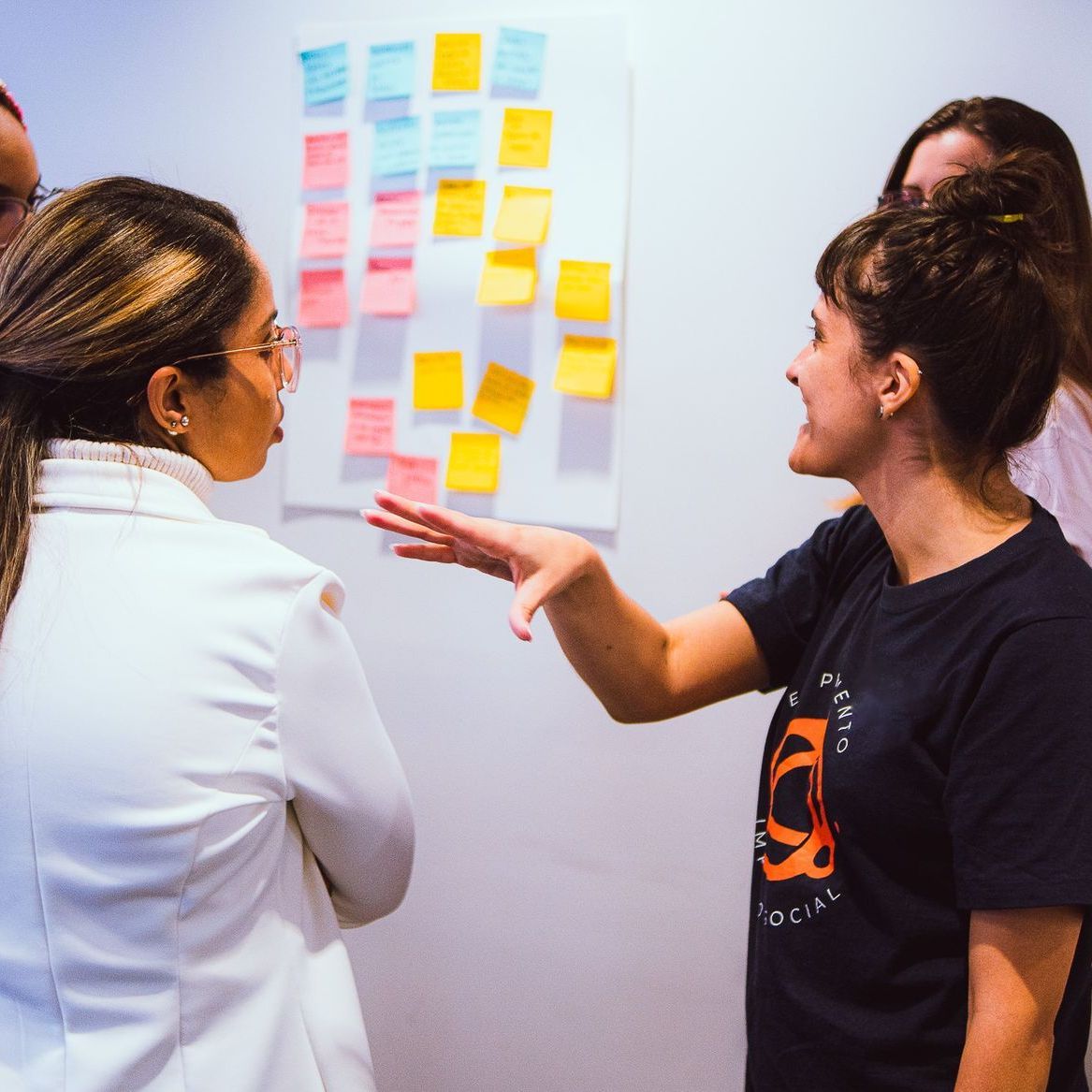 Duas pessoas conversando sobre post-its coloridos em uma parede em uma sala de reuniões.
