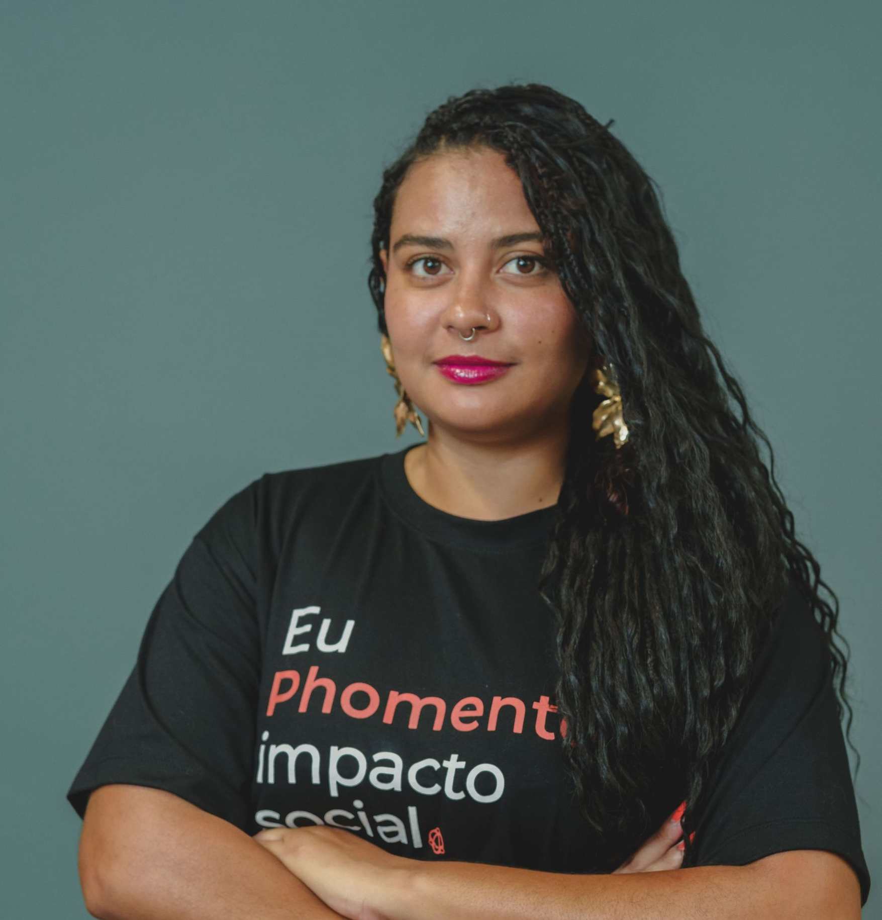 Mulher com camiseta preta com texto em português, em pé contra um fundo verde liso.