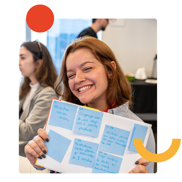 Uma pessoa sorridente segura um caderno coberto de notas adesivas azuis durante um workshop.