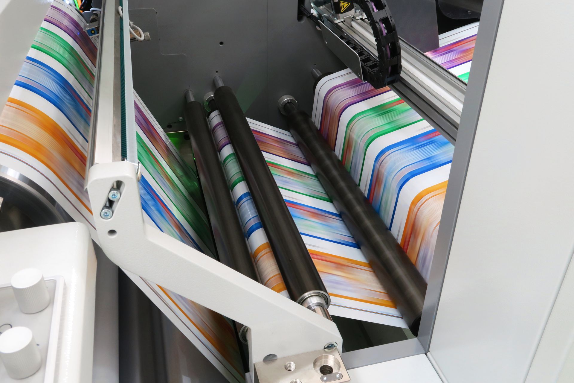 Commercial printing press rollers feeding brightly colored full-color printed sheets.
