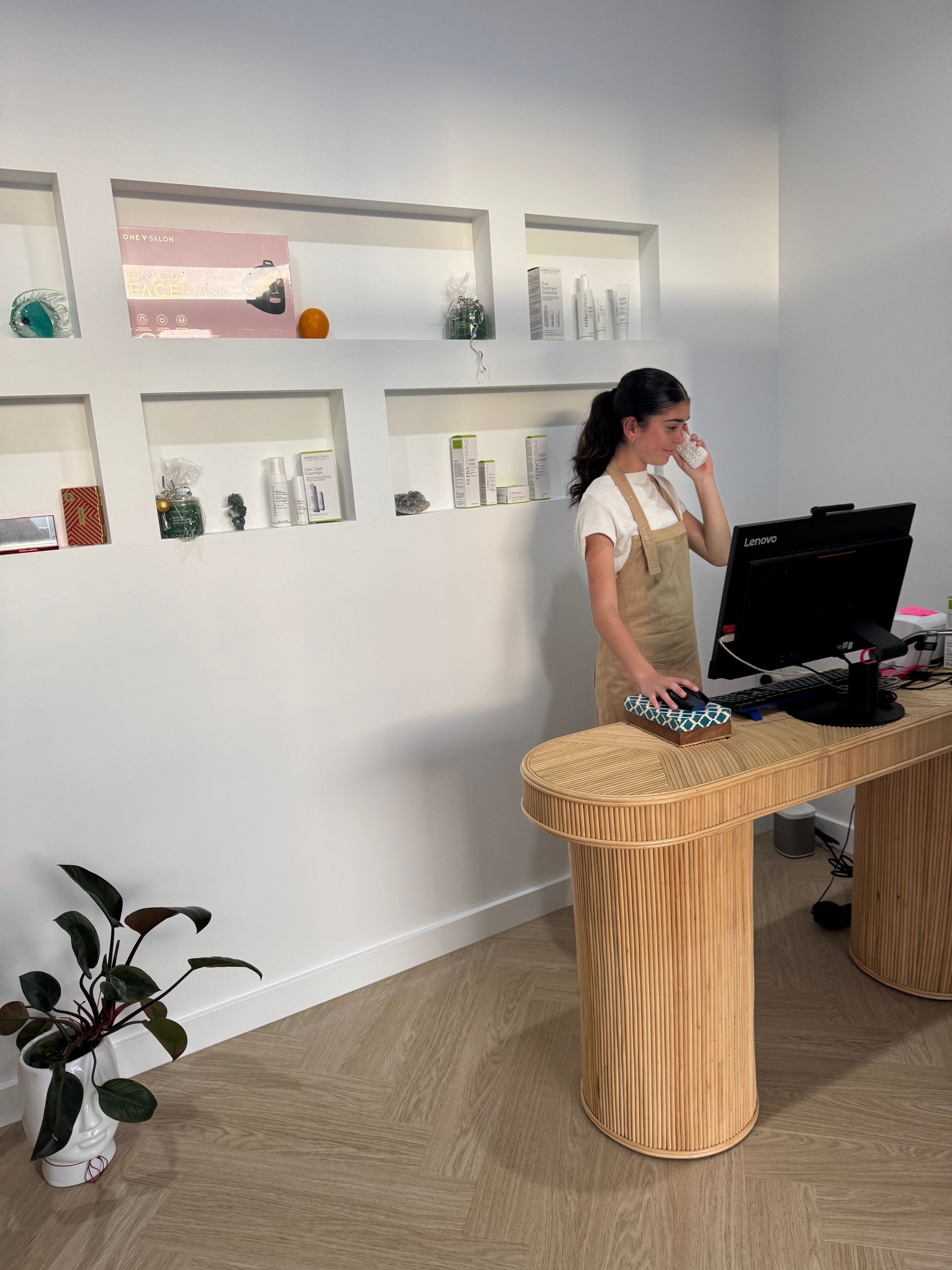 Woman in overalls on phone at wooden desk in bright office, built-in wall shelves — Aqua Marine Skin and Beauty in Tuncurry, NSW