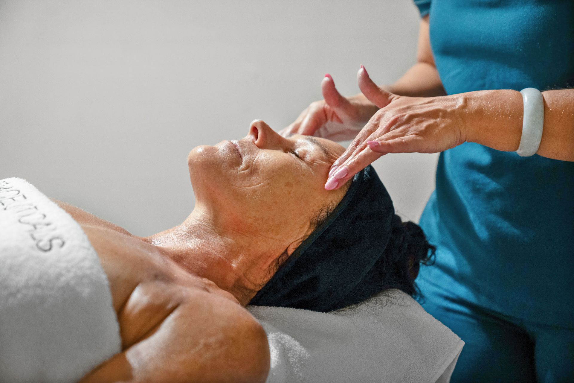 Person receiving a facial treatment with hands massaging their face, in a spa setting  — Aqua Marine Skin and Beauty in Tuncurry, NSW