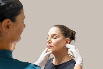 Woman Receiving Cosmetic Procedure on Her Face. Doctor in Gloves Holds Device Near Her Cheek — Aqua Marine Skin and Beauty in Tuncurry, NSW