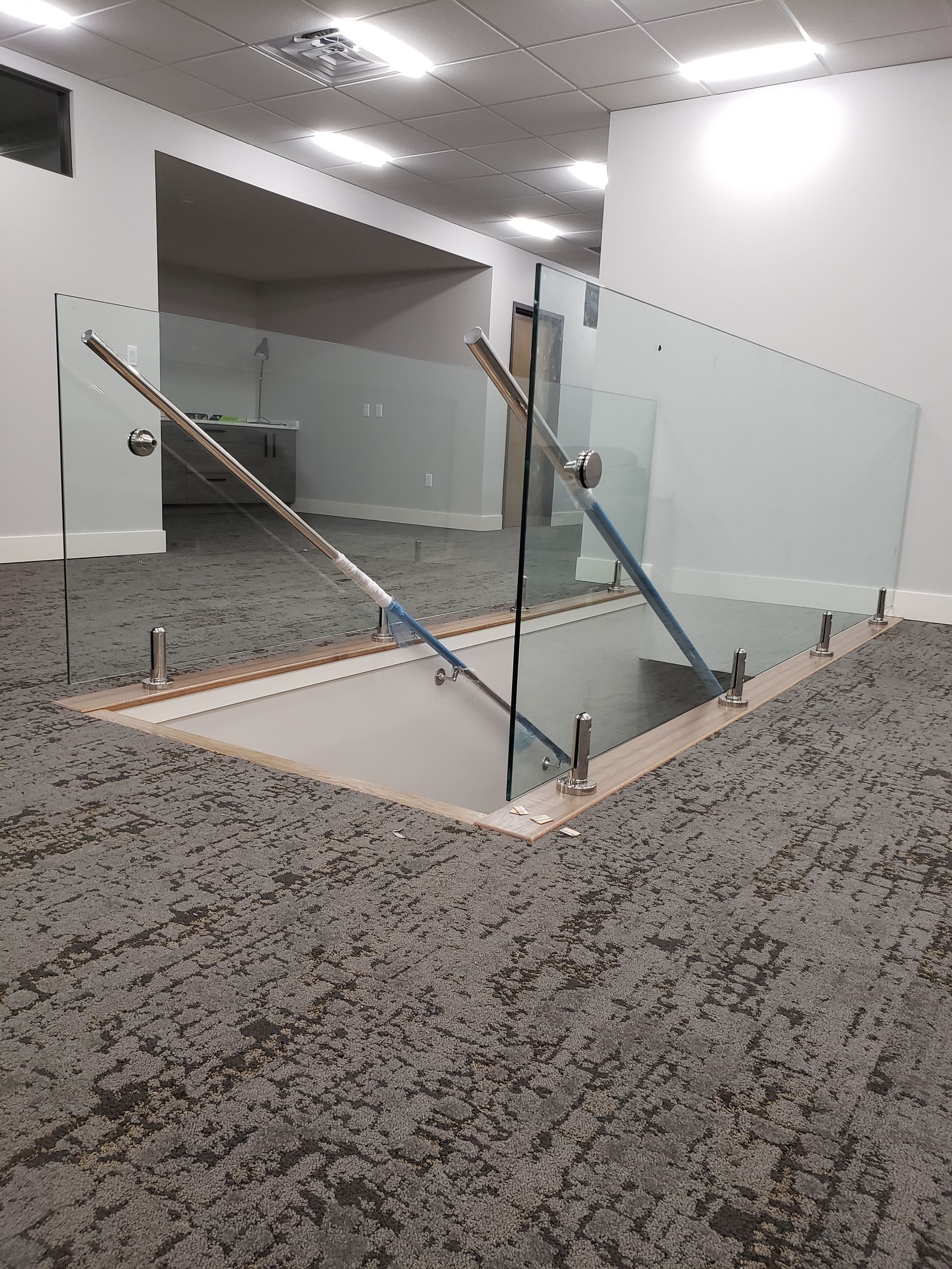 A staircase with a glass railing and a carpeted floor in a room.
