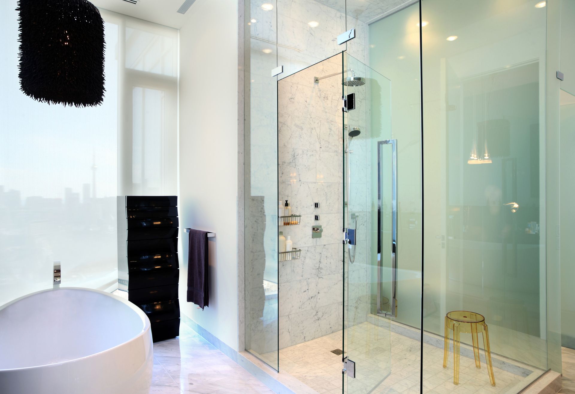 A modern bathroom featuring a white soaking tub, a large glass-enclosed marble shower, and a gold stool.