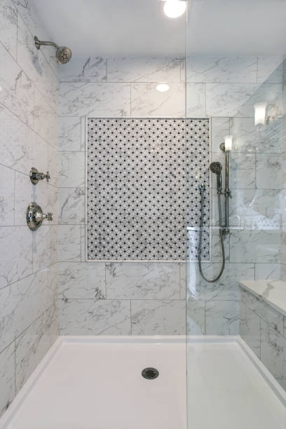 A marble-tiled walk-in shower with a patterned mosaic inlay, a handheld showerhead, and glass partition.