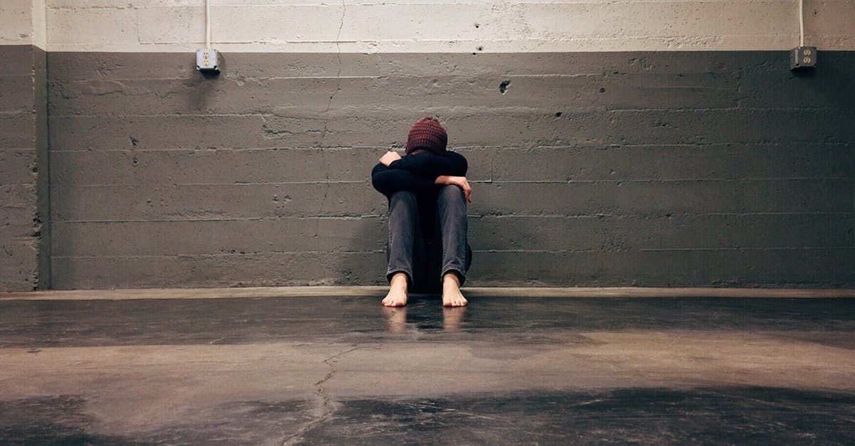 A man is sitting on the floor in a dark room with his head down.