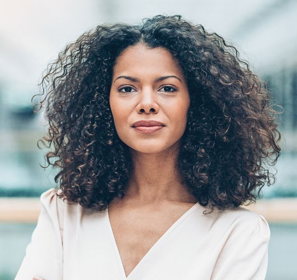 A woman with curly hair is wearing a white shirt and looking at the camera.