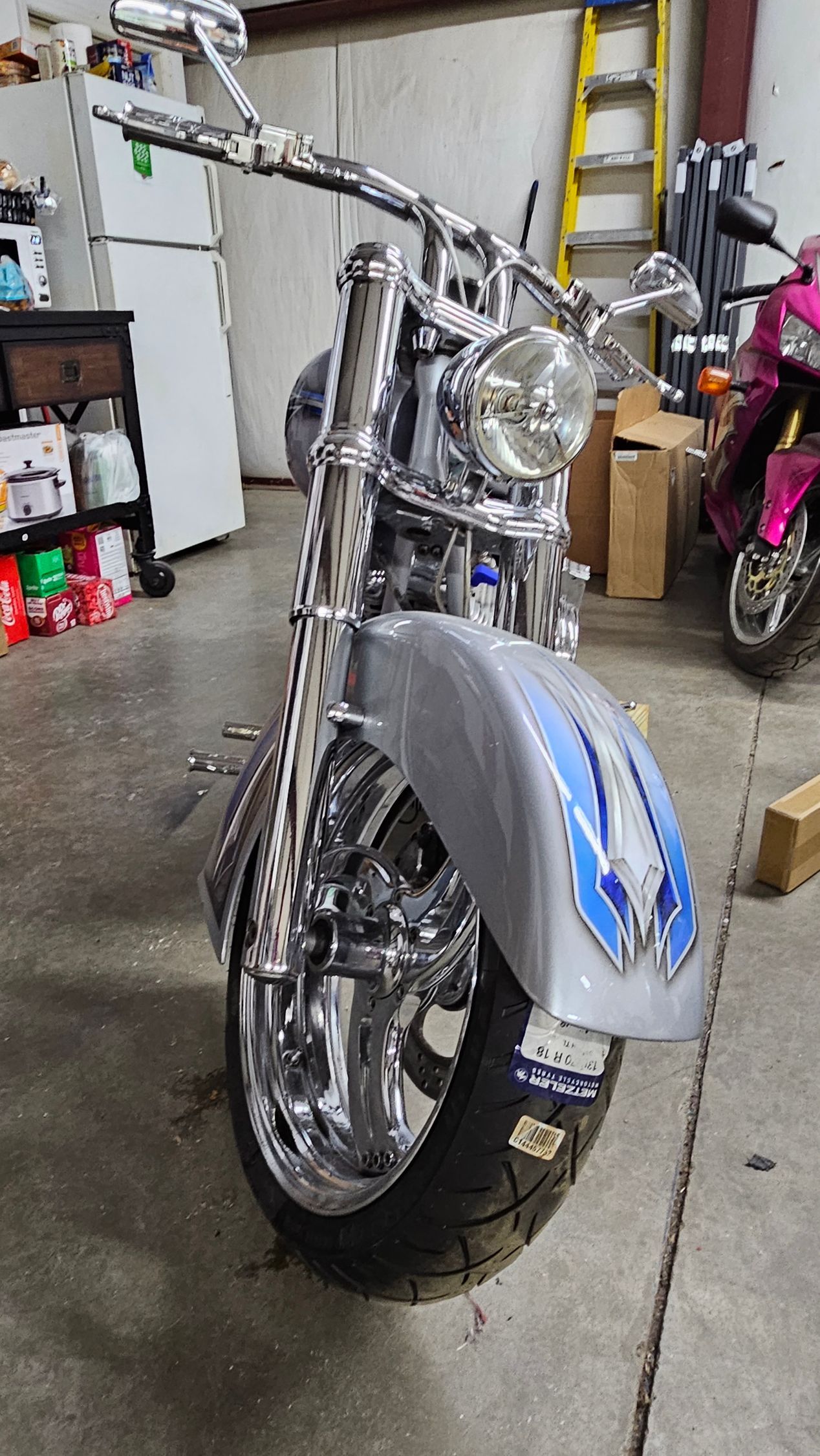 A motorcycle is parked in a garage next to a pink motorcycle.