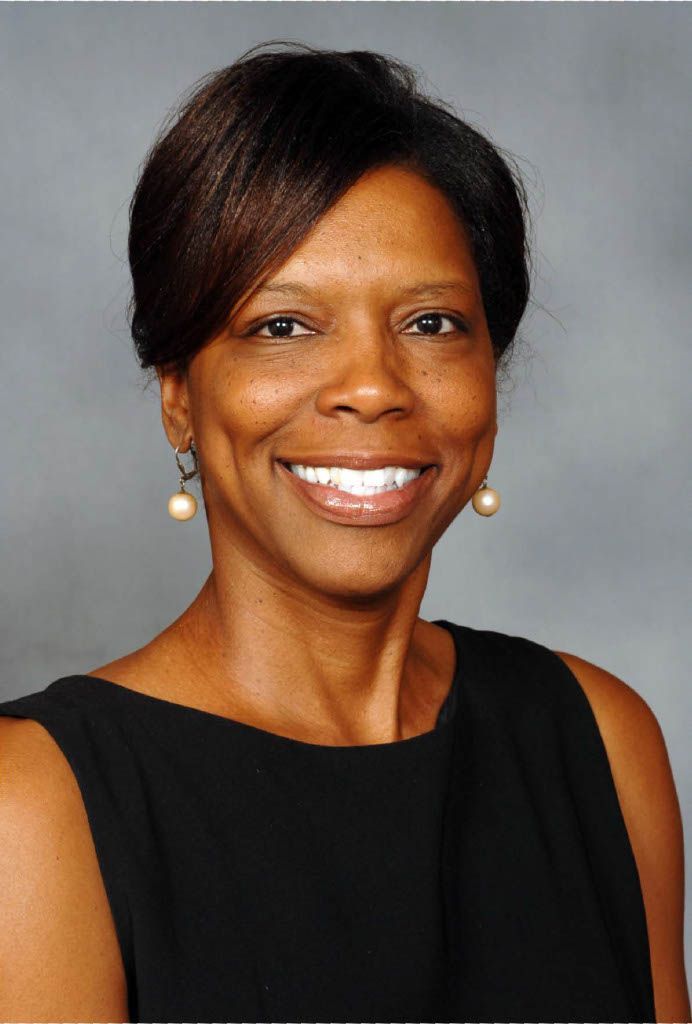 Smiling portrait of a person in a black sleeveless top against a gray studio background