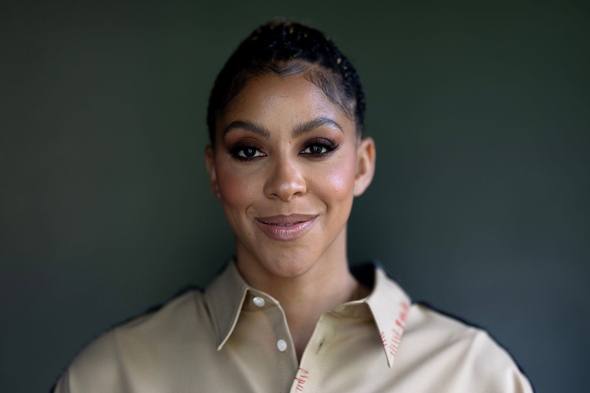 Portrait of a smiling person in a beige shirt against a dark green background