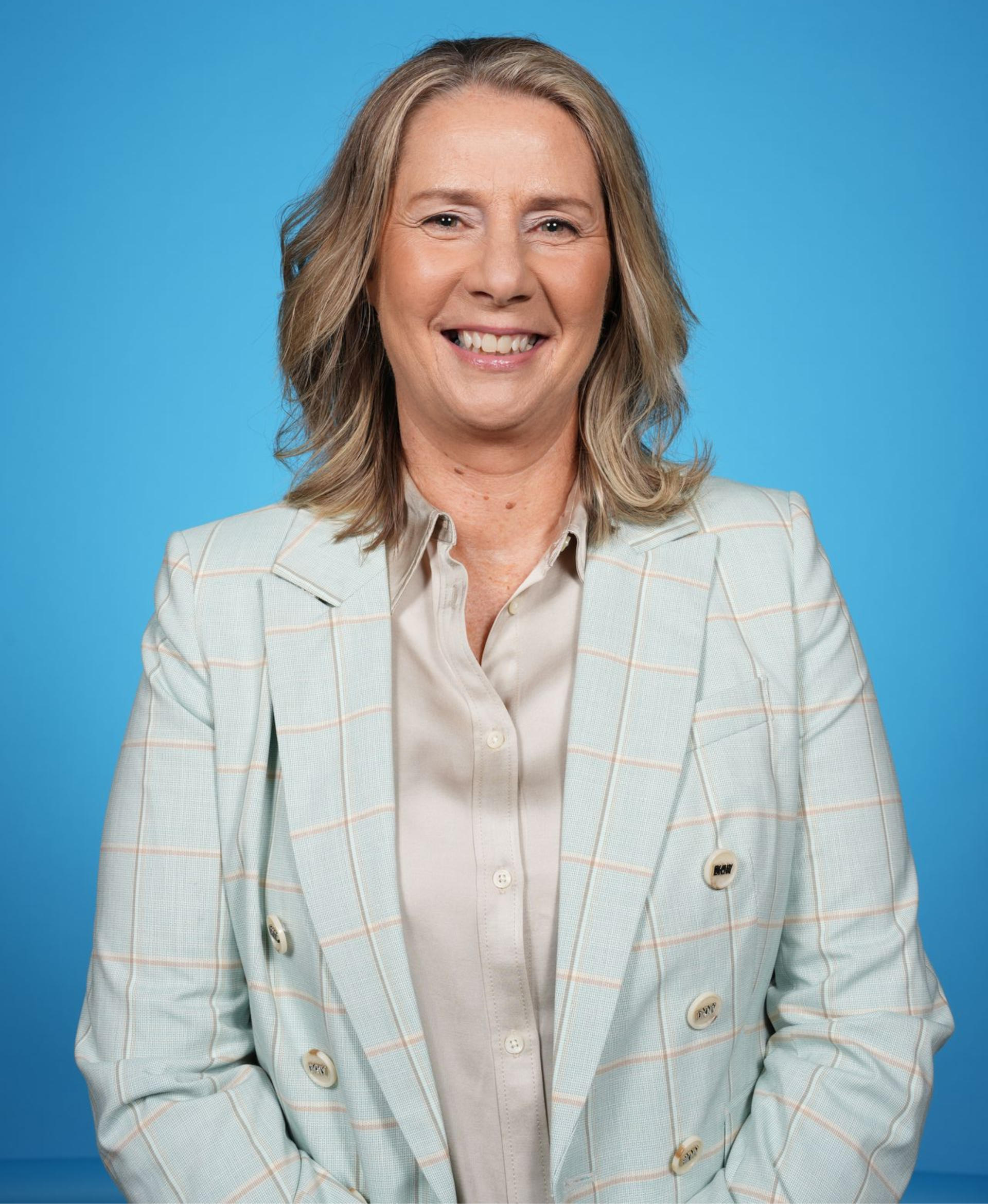 Smiling person in a light blue blazer and white blouse against a blue background