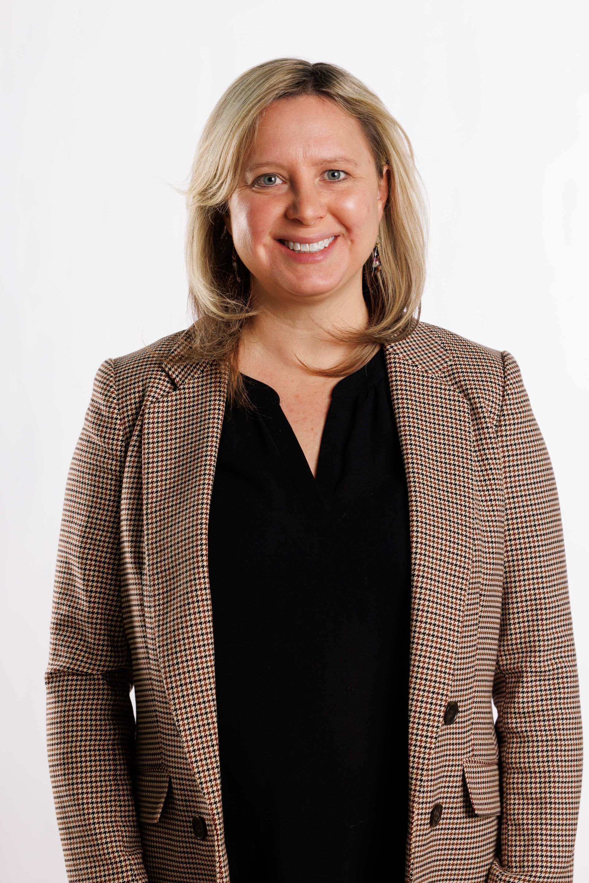Portrait of a smiling person in a black top and patterned blazer against a white background