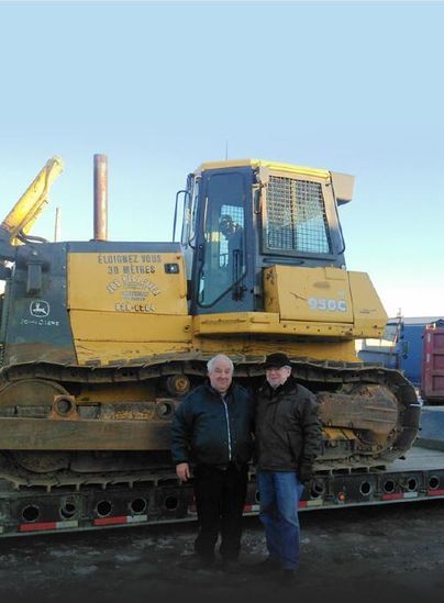 Deux hommes se tiennent devant un gros bulldozer jaune.