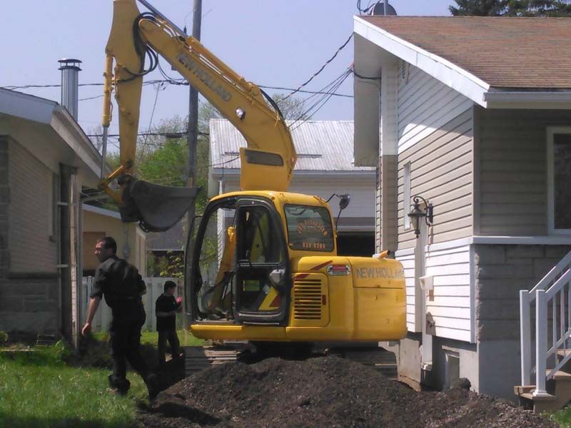 Une excavatrice jaune creuse un trou devant une maison