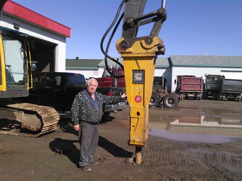 Un homme debout à côté d’une excavatrice jaune portant le numéro 7